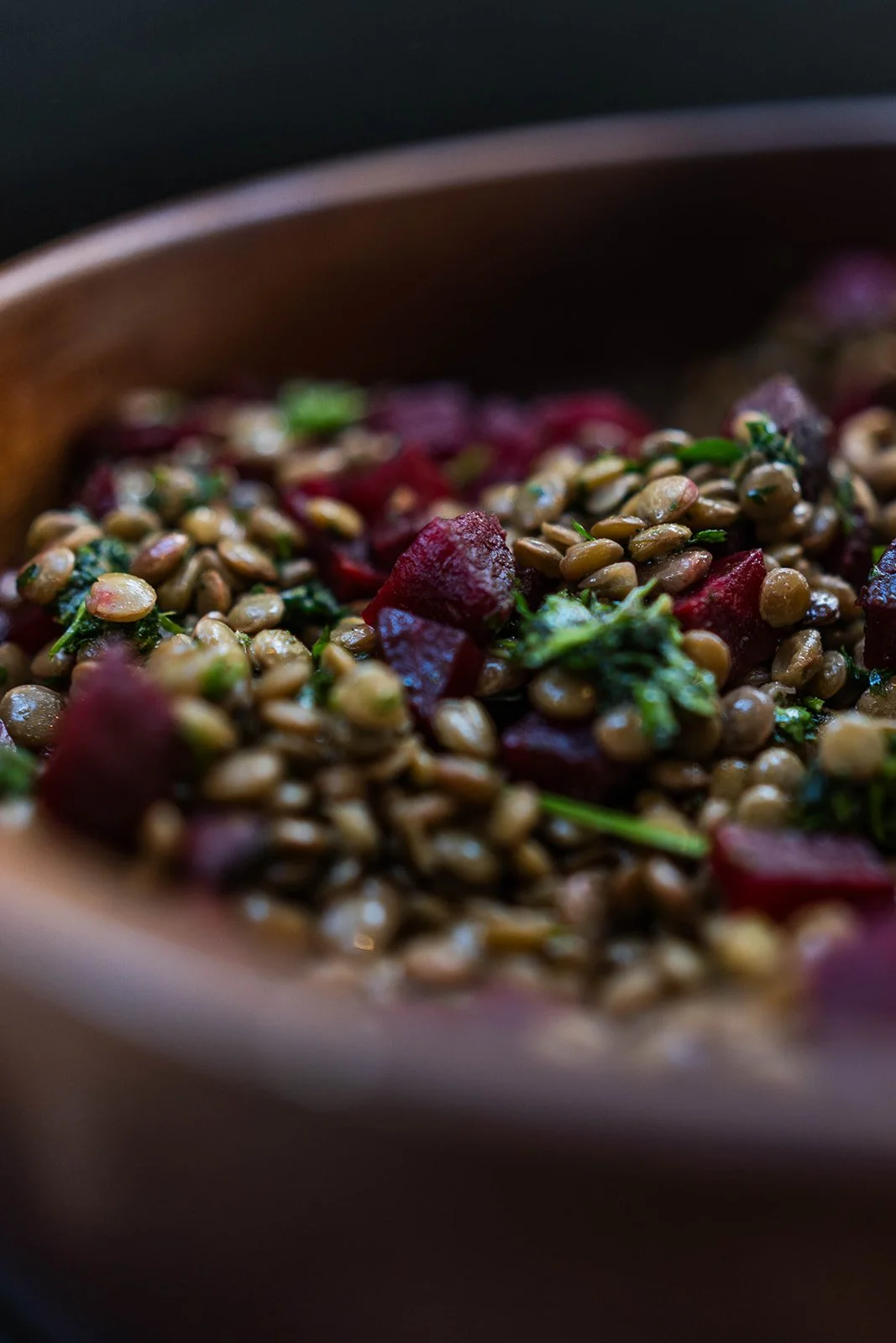 Close-up of a lentil salad with beets and greens in a wooden bowl.