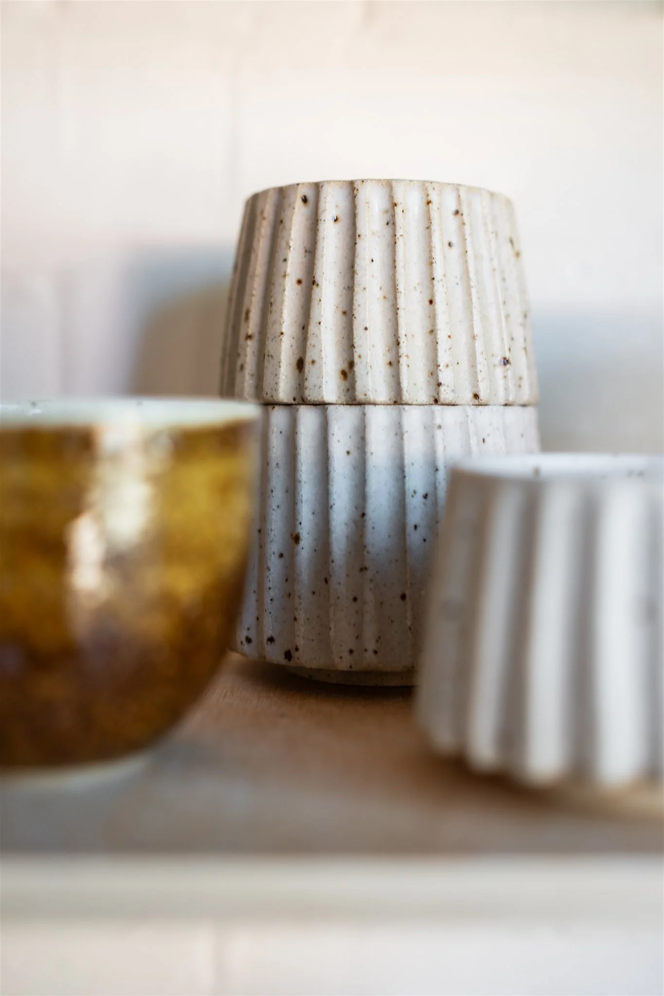 Close-up of various ceramic containers with vertical ridges, including a beige vase and a small bowl, on a wooden surface.