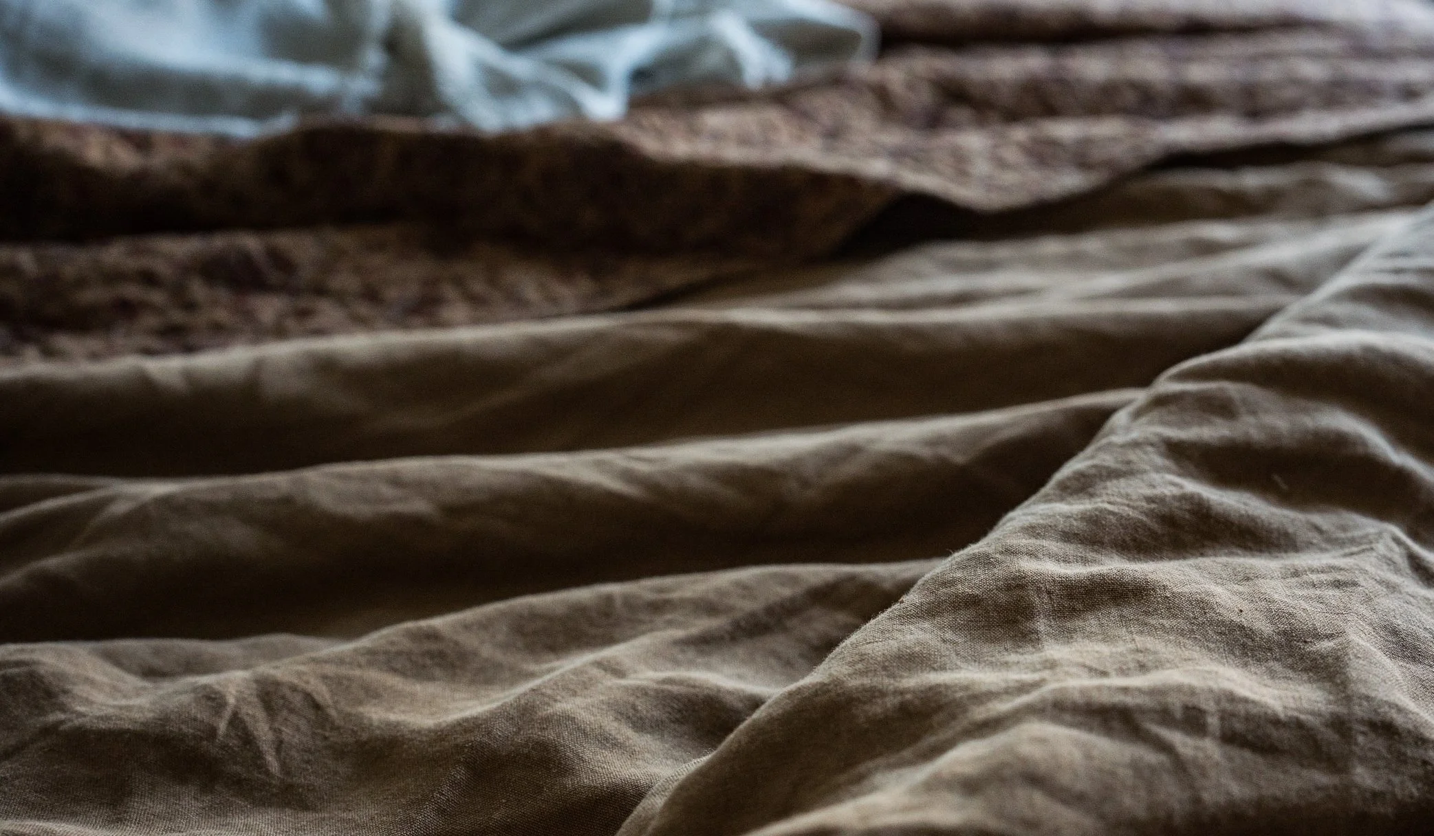 Close-up of rumpled bed sheets with a bedspread and blankets in neutral colors.