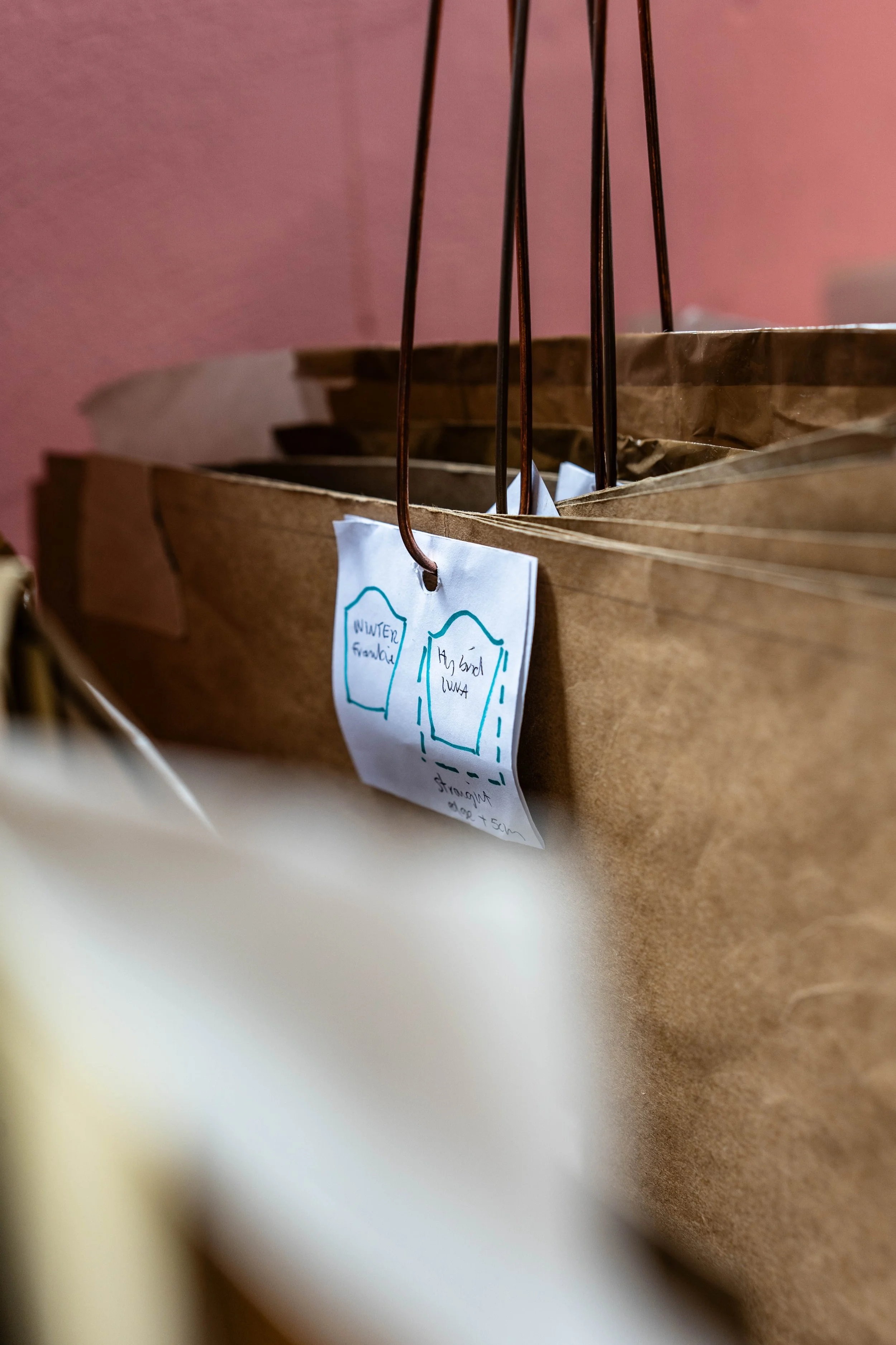 A brown paper grocery bag with handwritten tags hanging from metal hooks.