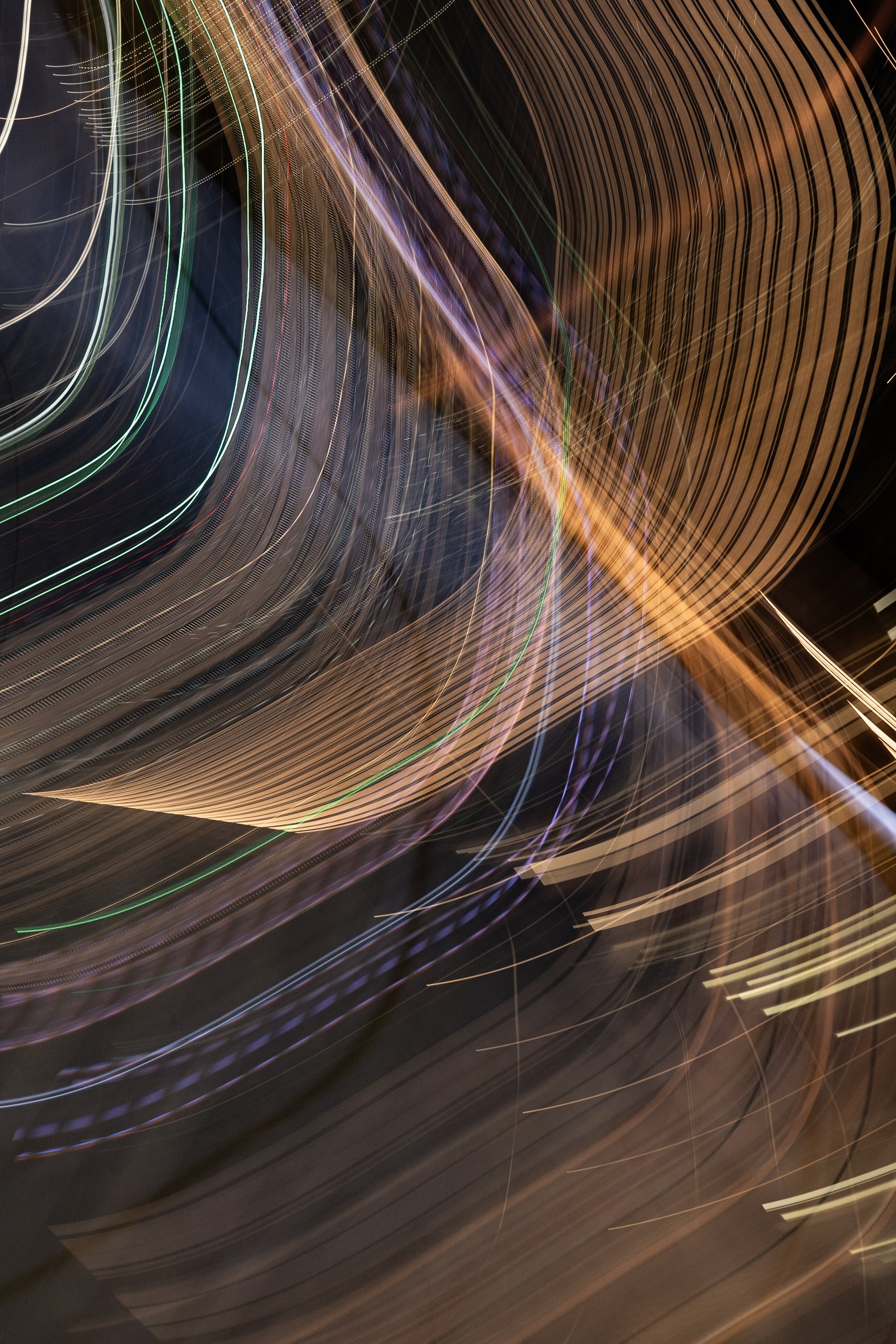 Abstract long exposure photo with colorful light trails and streaks forming curved and straight lines against a dark background.