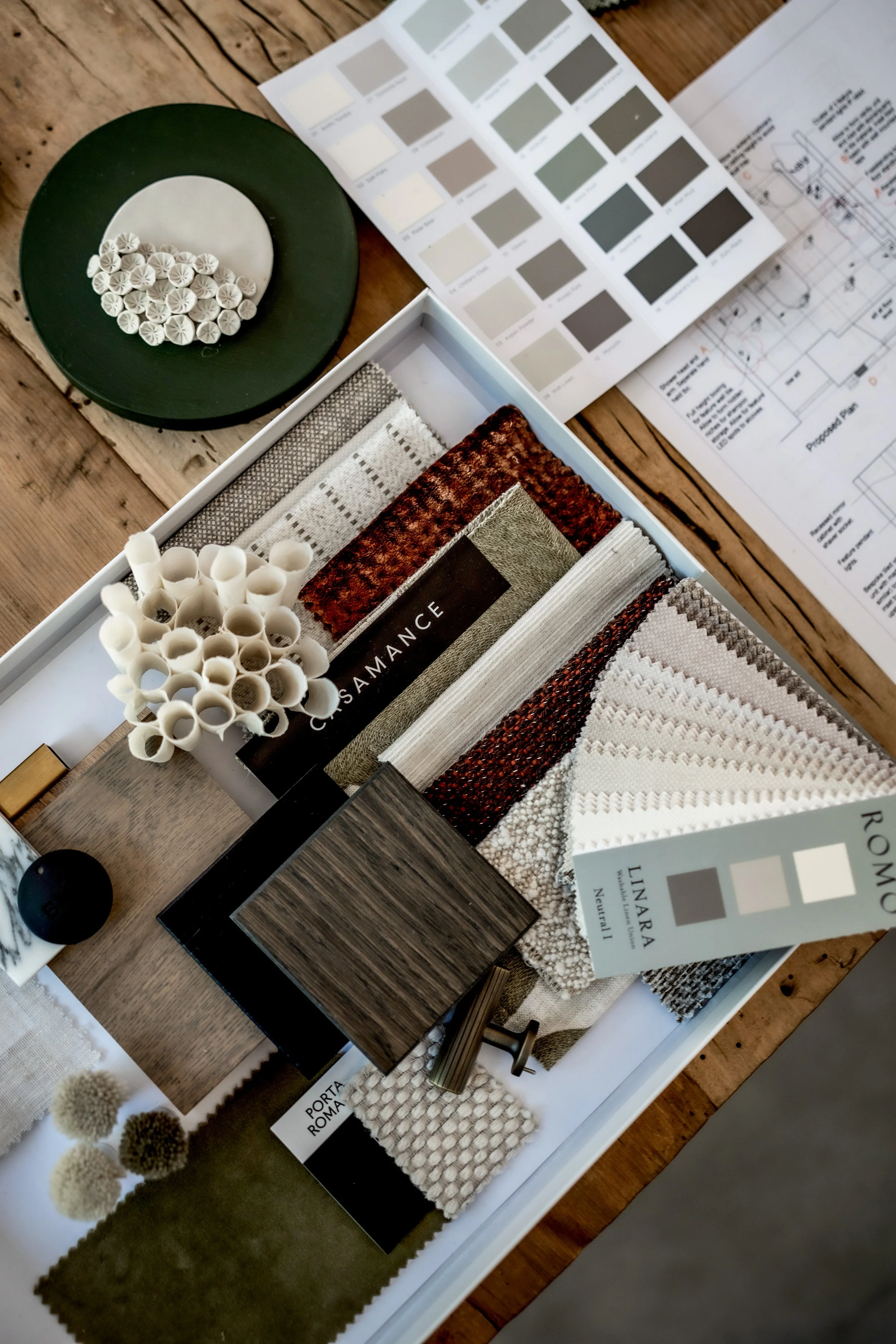 A collection of fabric samples, color swatches, and design materials on a table, along with architectural plans and color charts.