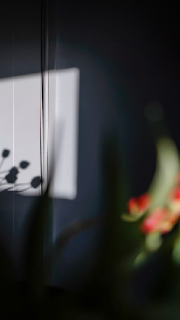 Close-up of a dark refrigerator with a white note attached, and blurred red flowers in the foreground.
