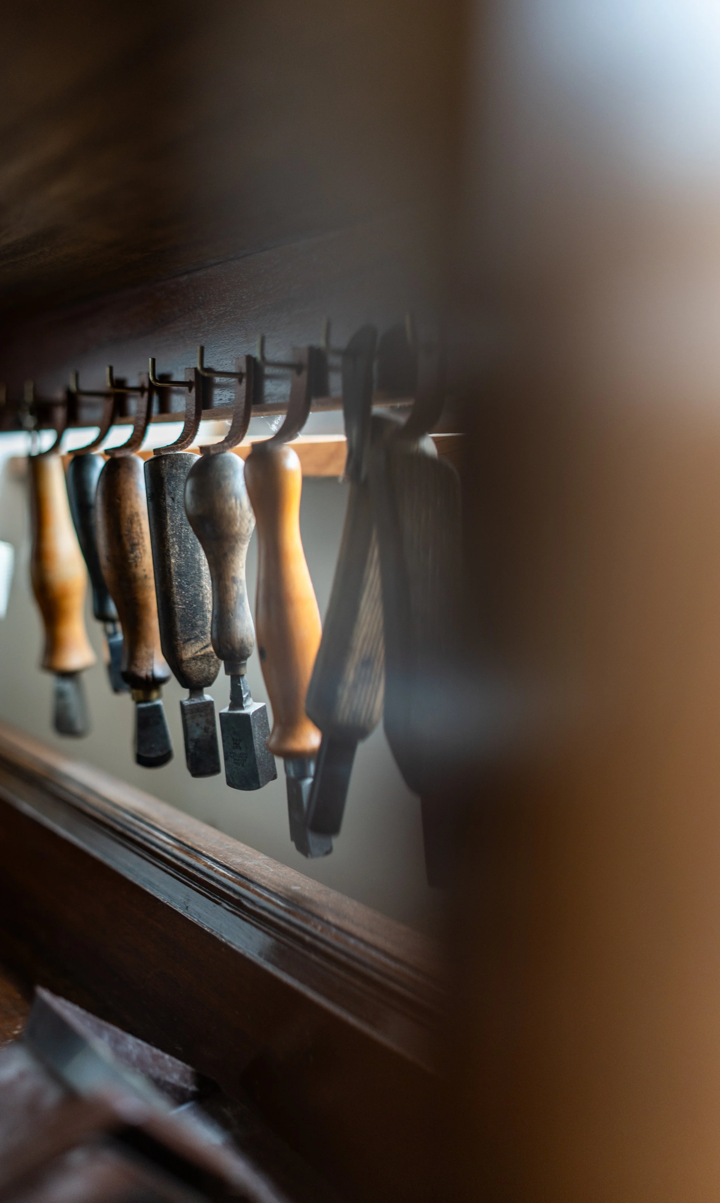Collection of woodworking chisels hanging on a wooden rack.