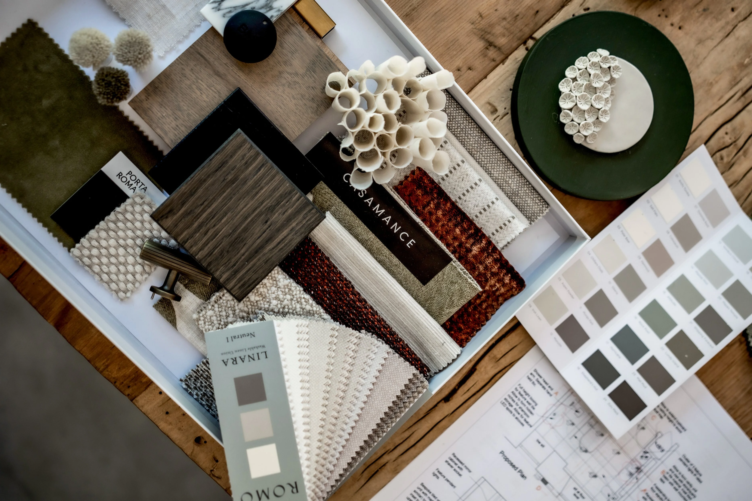 Interior design sample board with fabric swatches, paint color samples, and design materials on a wooden table.