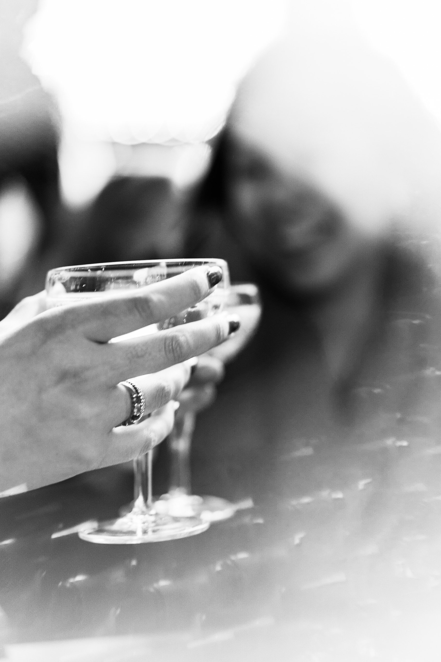 A close-up black and white photo of a hand holding a glass of wine on a table