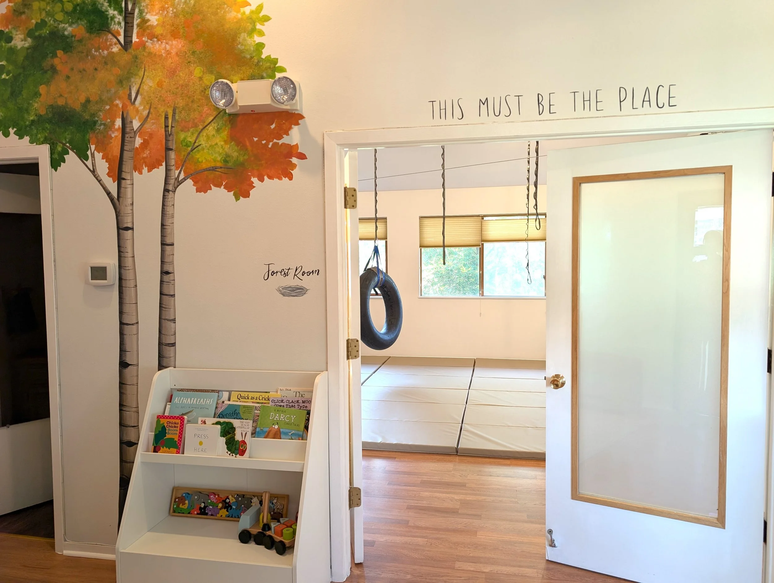 Speech therapy open door with bookshelf and trees painted on wall