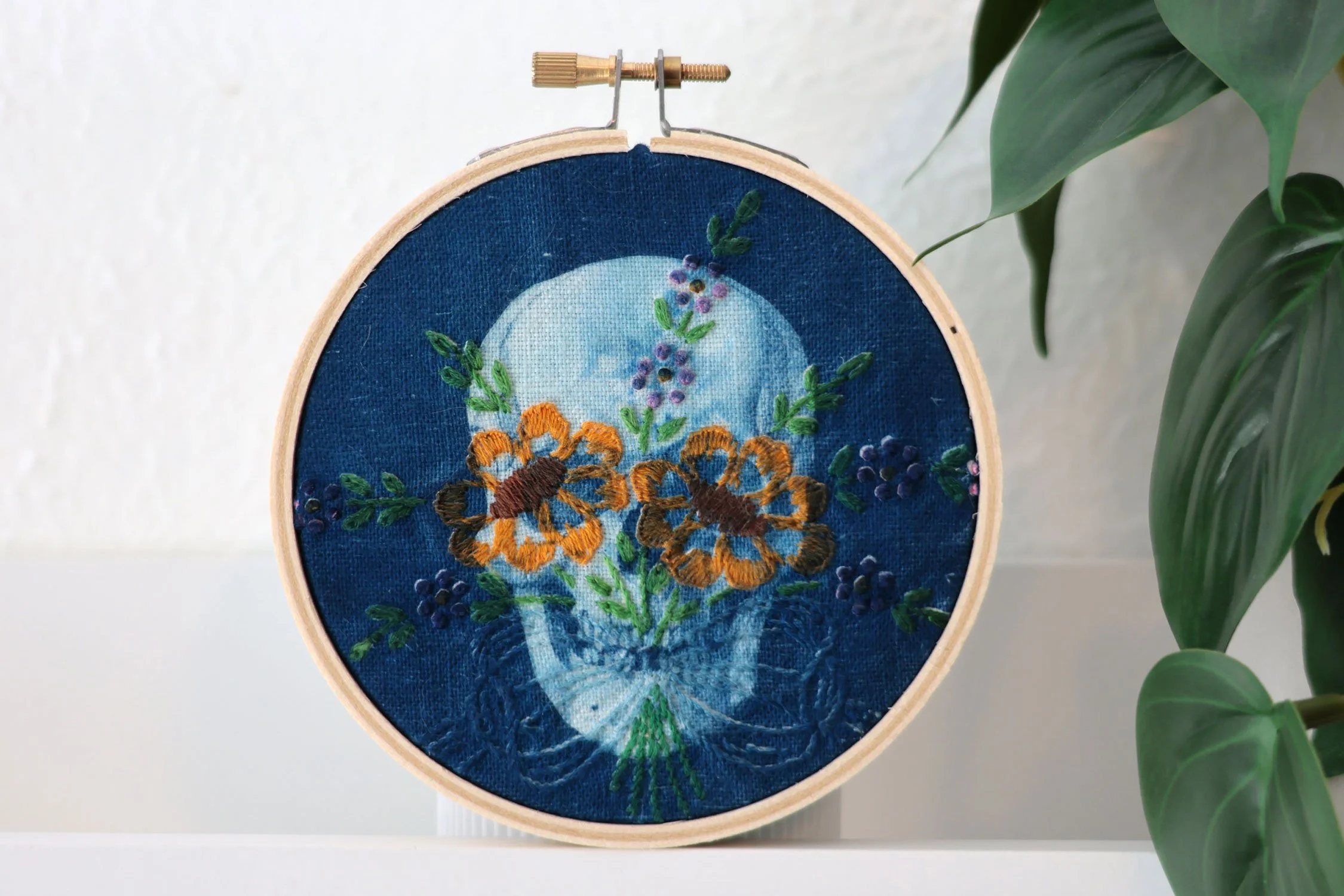 Cyanotype of a skull on a vintage embroidered linen. There are flowers on the eye sockets.