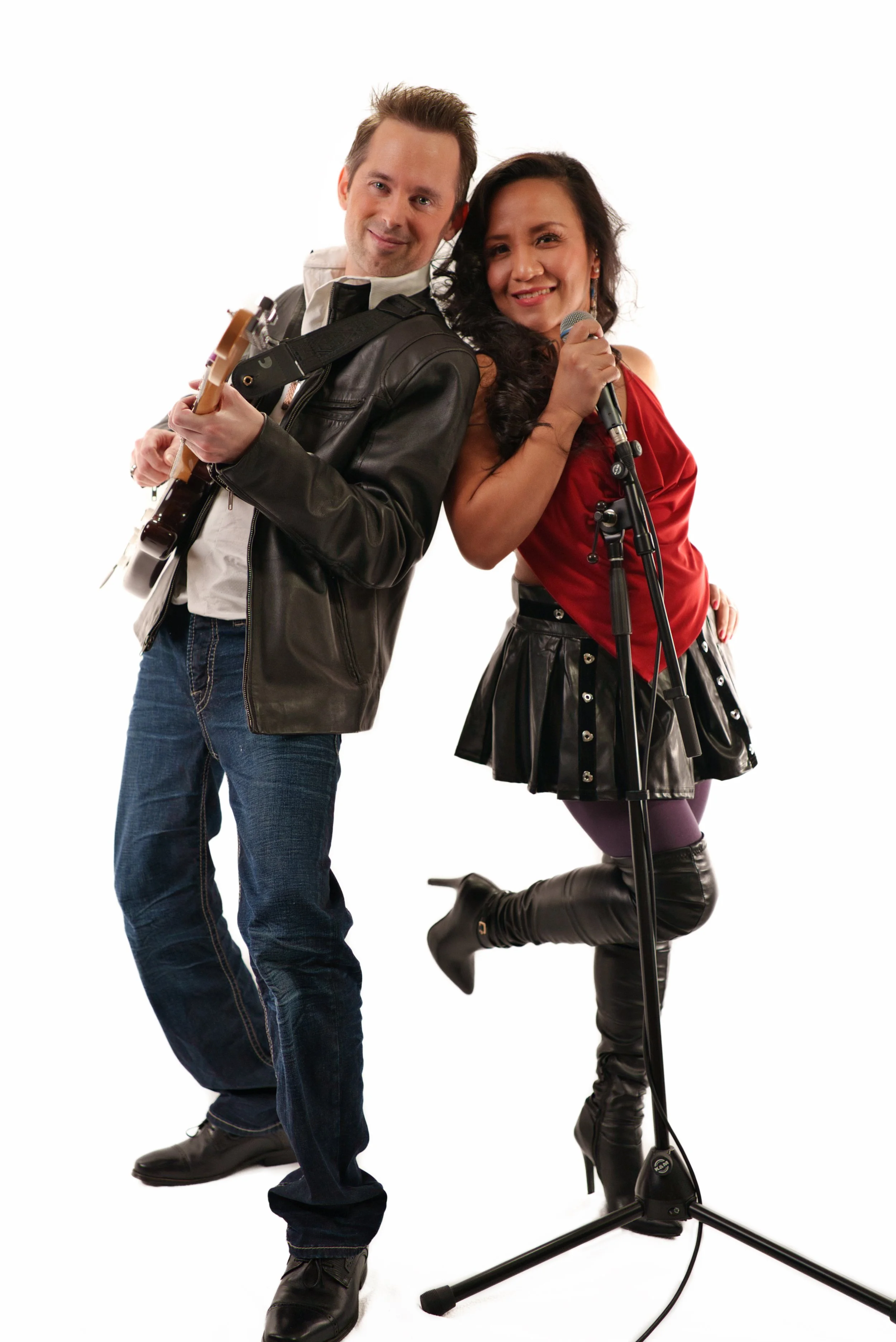 A man playing guitar and a woman singing into a microphone, positioned back to back, against a white background.