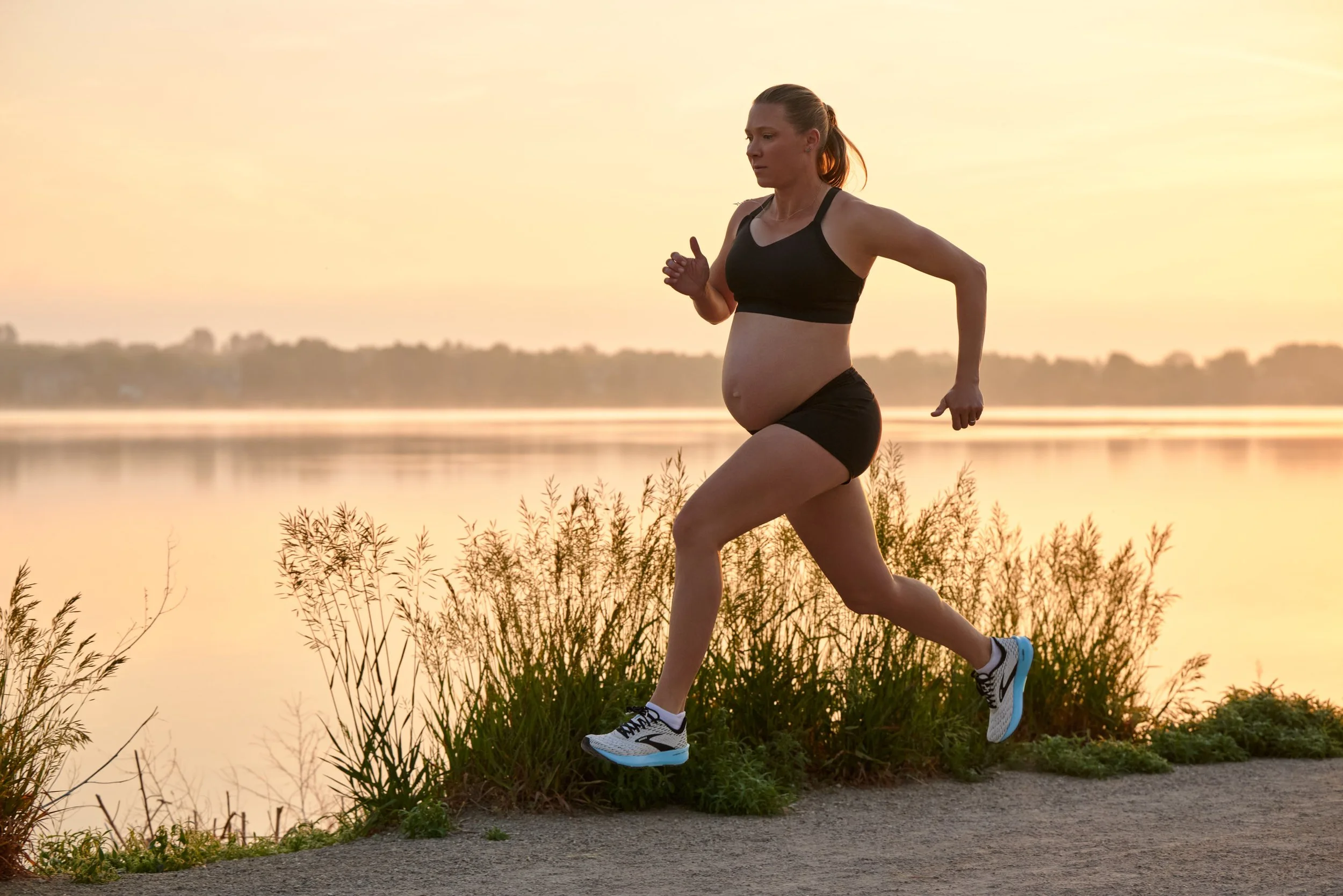 Pregnant runner striding along a lakeside path at golden hour, editorial photography for Outside Magazine