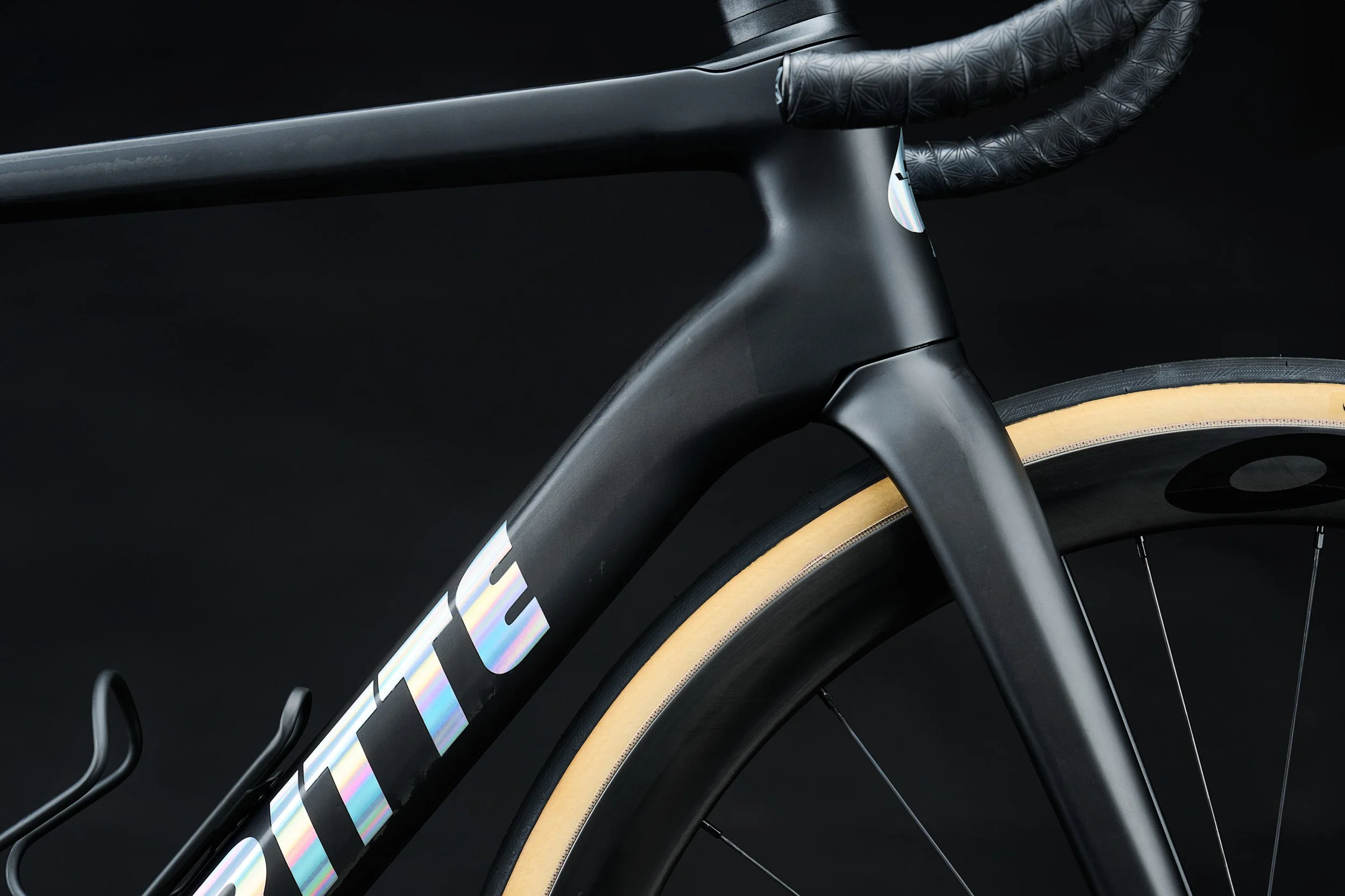 Macro of the Ritte Esprit carbon frame with holographic logo and tan-wall tire, studio product photography for Ritte Cycles