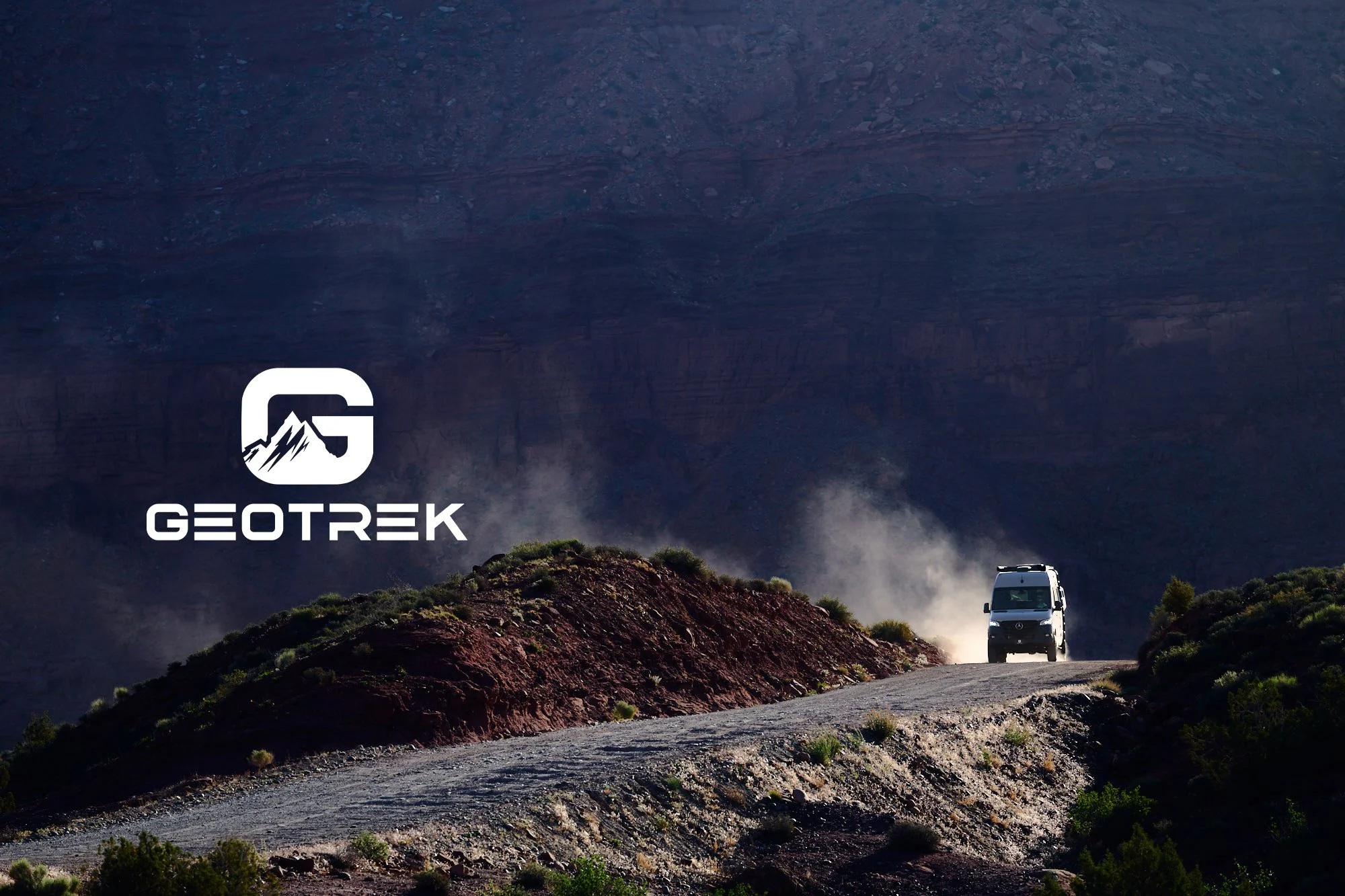 Commercial photo of Geotrek Flatiron camper van driving a dusty Moab, Utah road at dusk