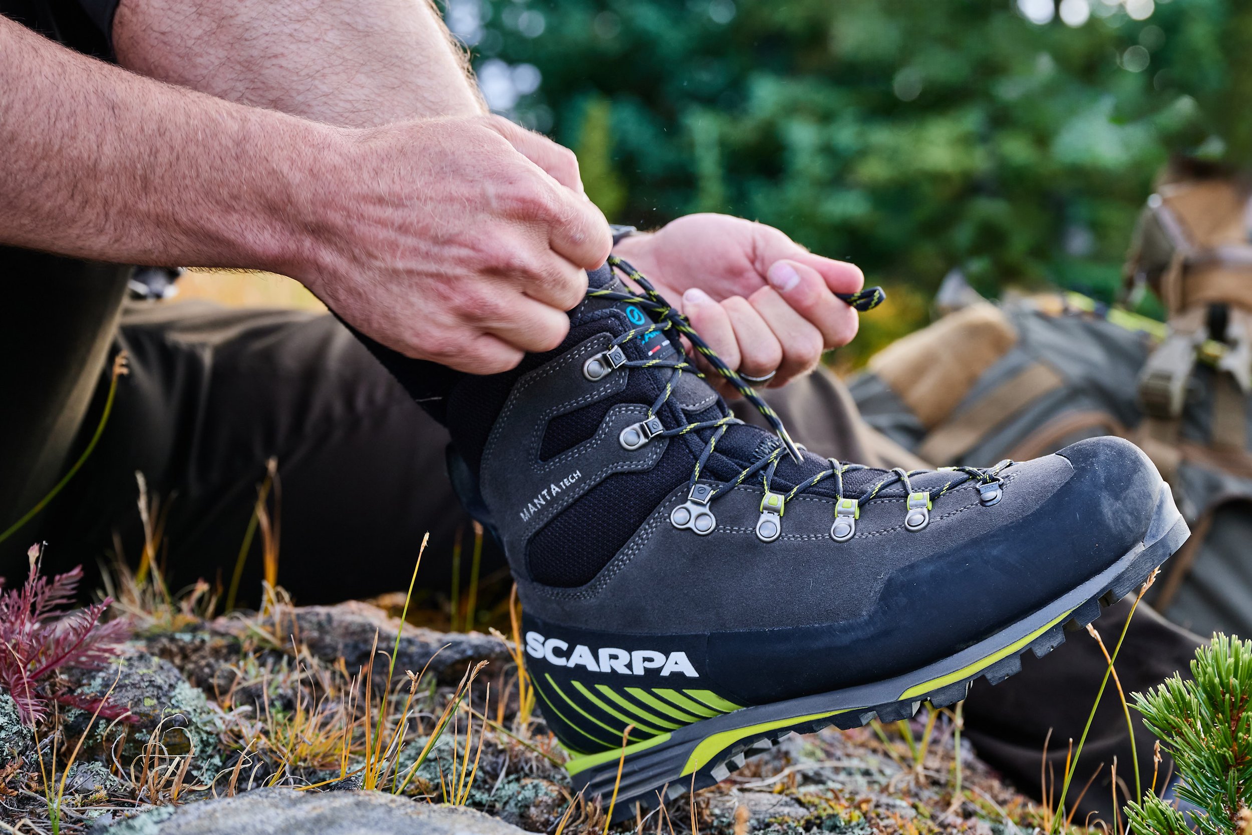 Hunter lacing a SCARPA boot at the trailhead with a pack behind, hunting footwear campaign photography for SCARPA