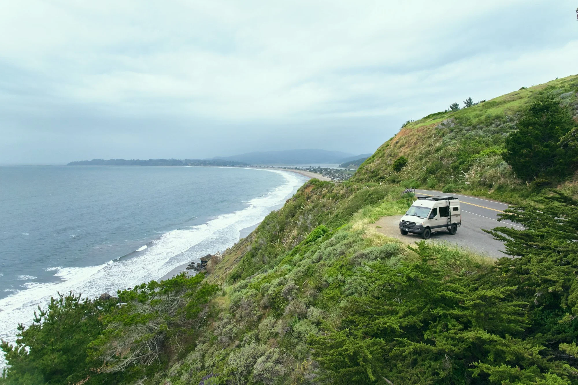 Aerial of a Geotrek camper van parked on a coastal cliff road above the ocean, adventure vehicle photography for Geotrek