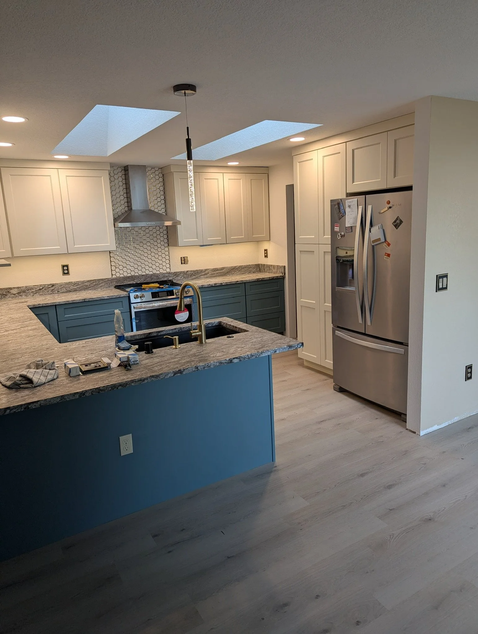Modern kitchen with blue island, white cabinets, stainless steel refrigerator, and skylights.