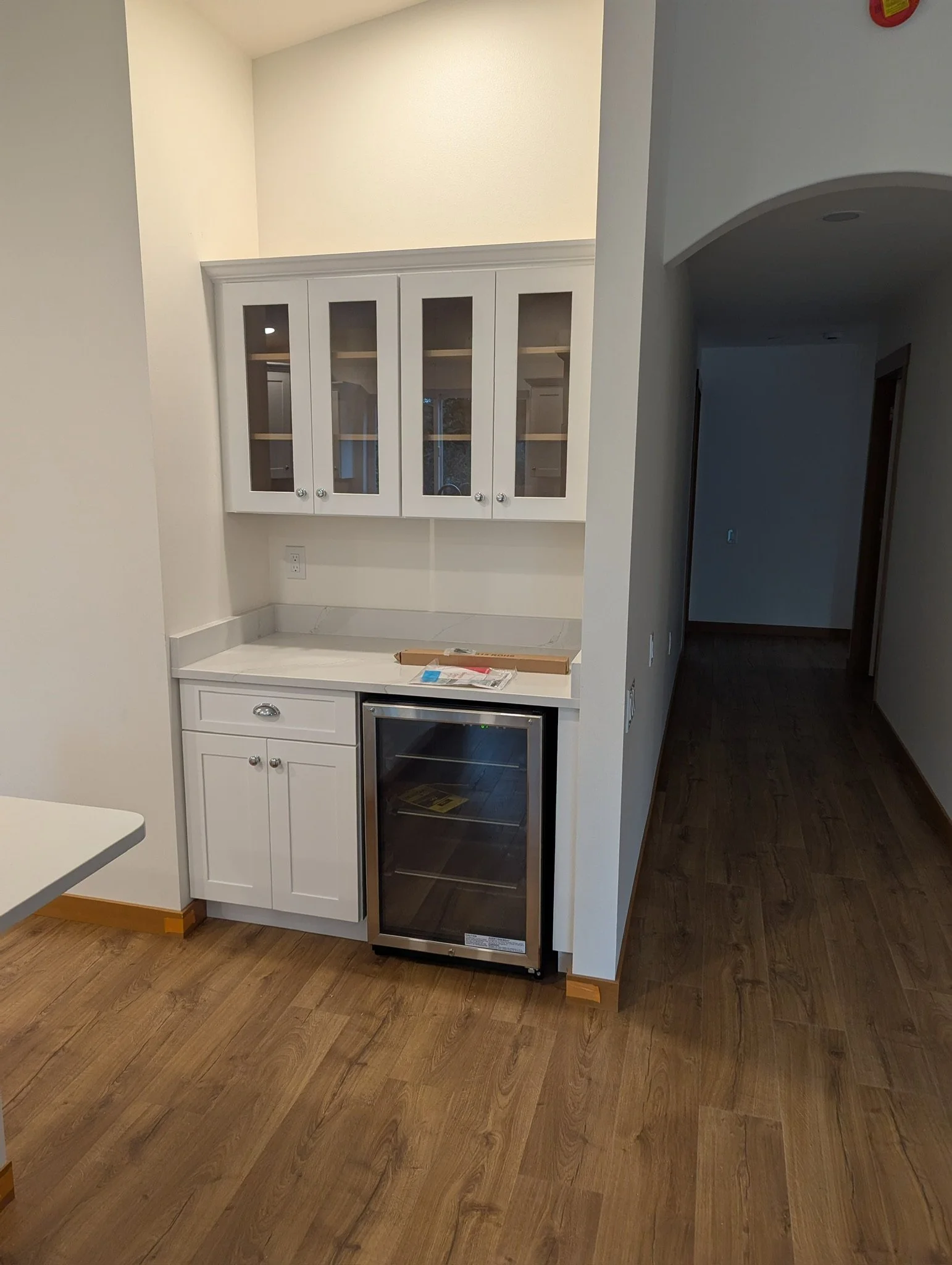 Kitchen nook with white cabinets, a marble countertop, and a wine cooler, with hardwood flooring.
