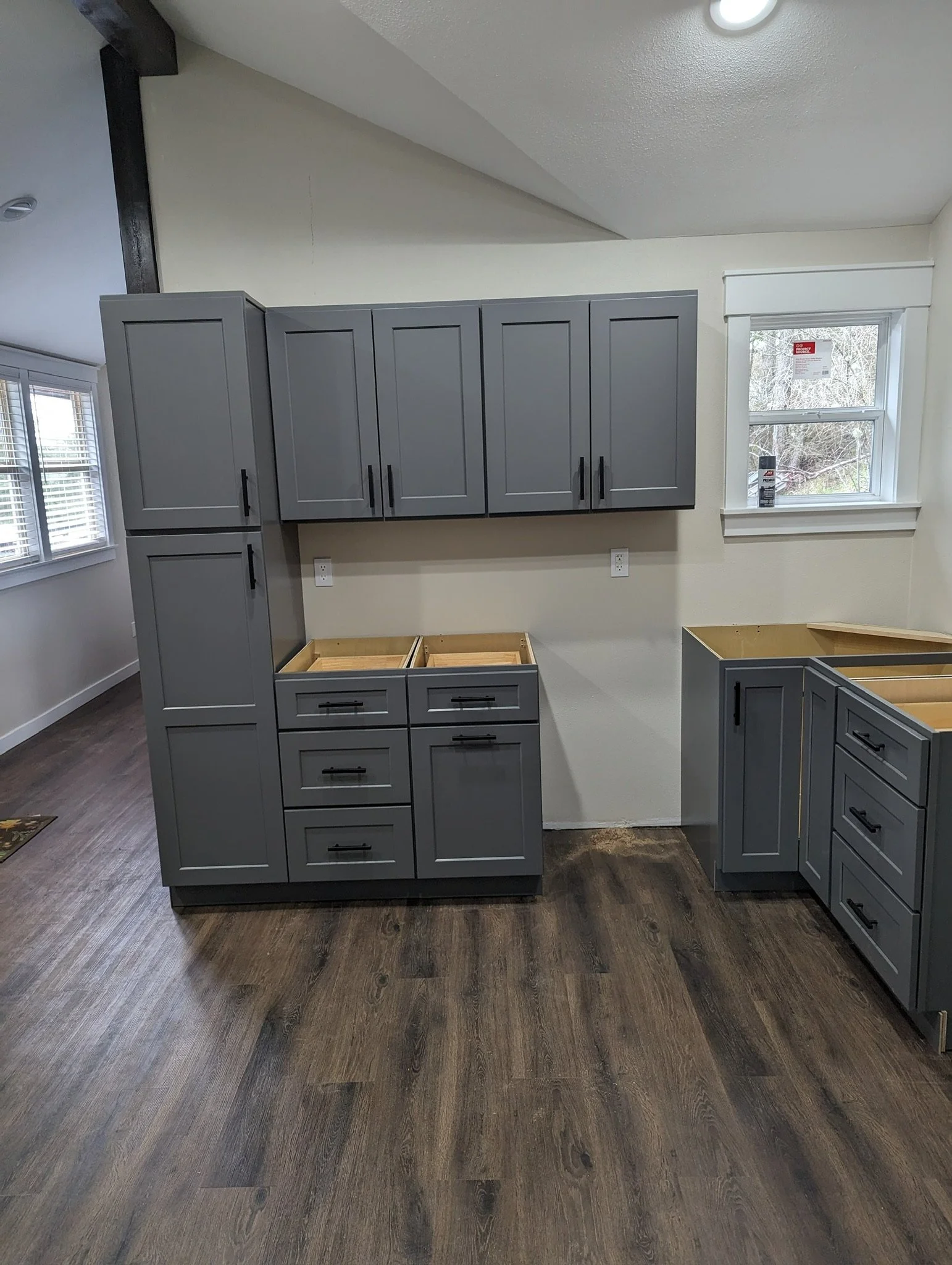Interior of a kitchen under construction with gray cabinets, some missing drawers, and dark wood flooring.