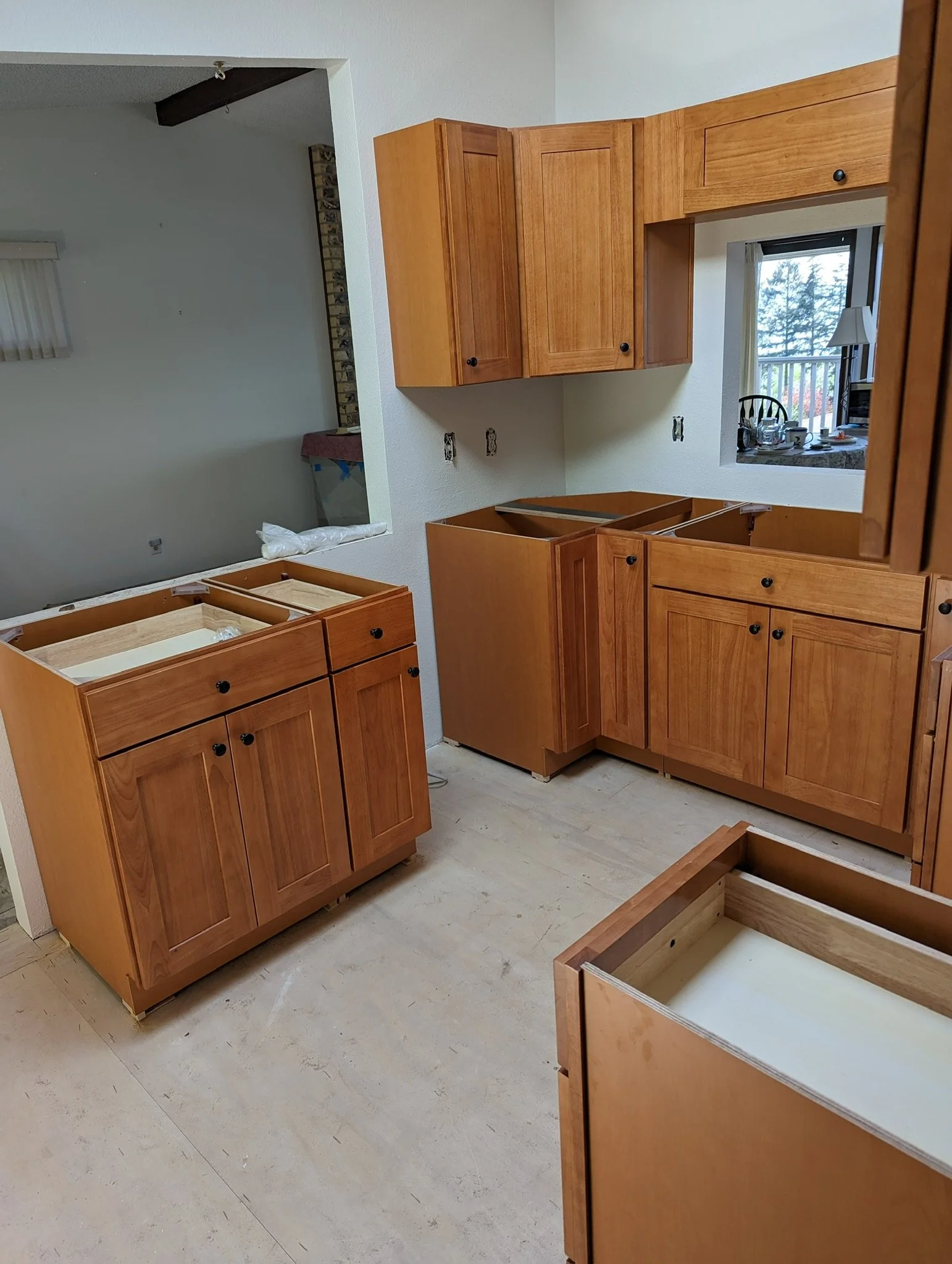 Kitchen with wooden cabinets under renovation, some cabinets are missing doors, and the floor is unfinished.