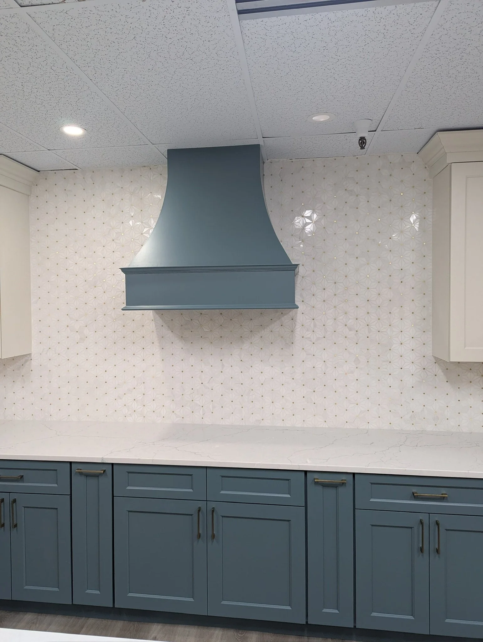 Blue kitchen cabinets with silver handles, white marble countertop, decorative patterned wall, and a blue range hood in the kitchen.
