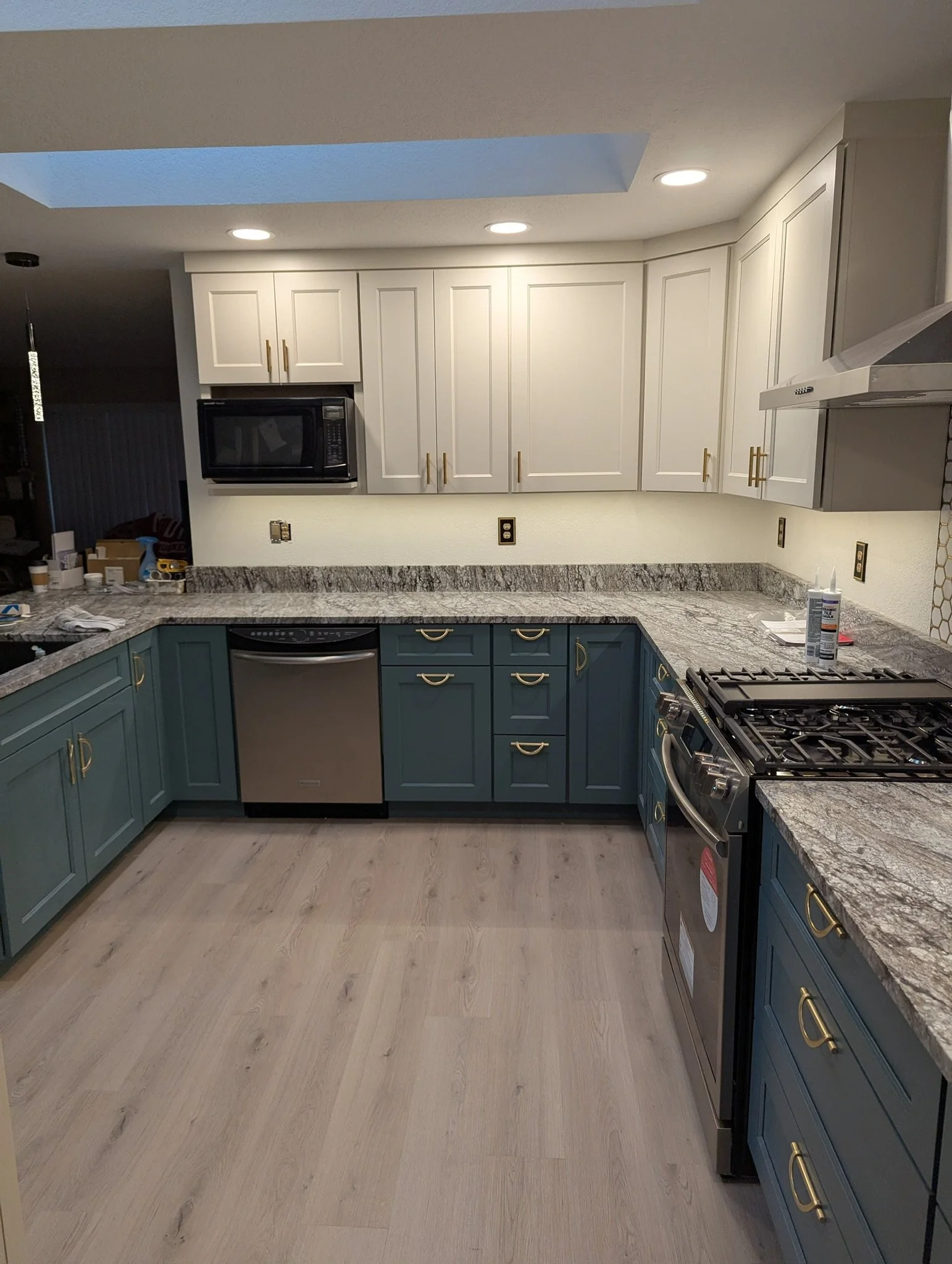 Modern kitchen with white upper cabinets, teal lower cabinets, granite countertops, and stainless steel appliances.