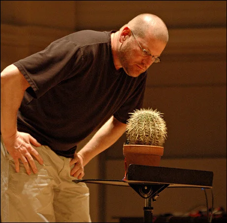 Paul Rudy is standing over a golden ball cactus on stage getting ready to play his composition Degrees of Separation, Grandchild of Tree.