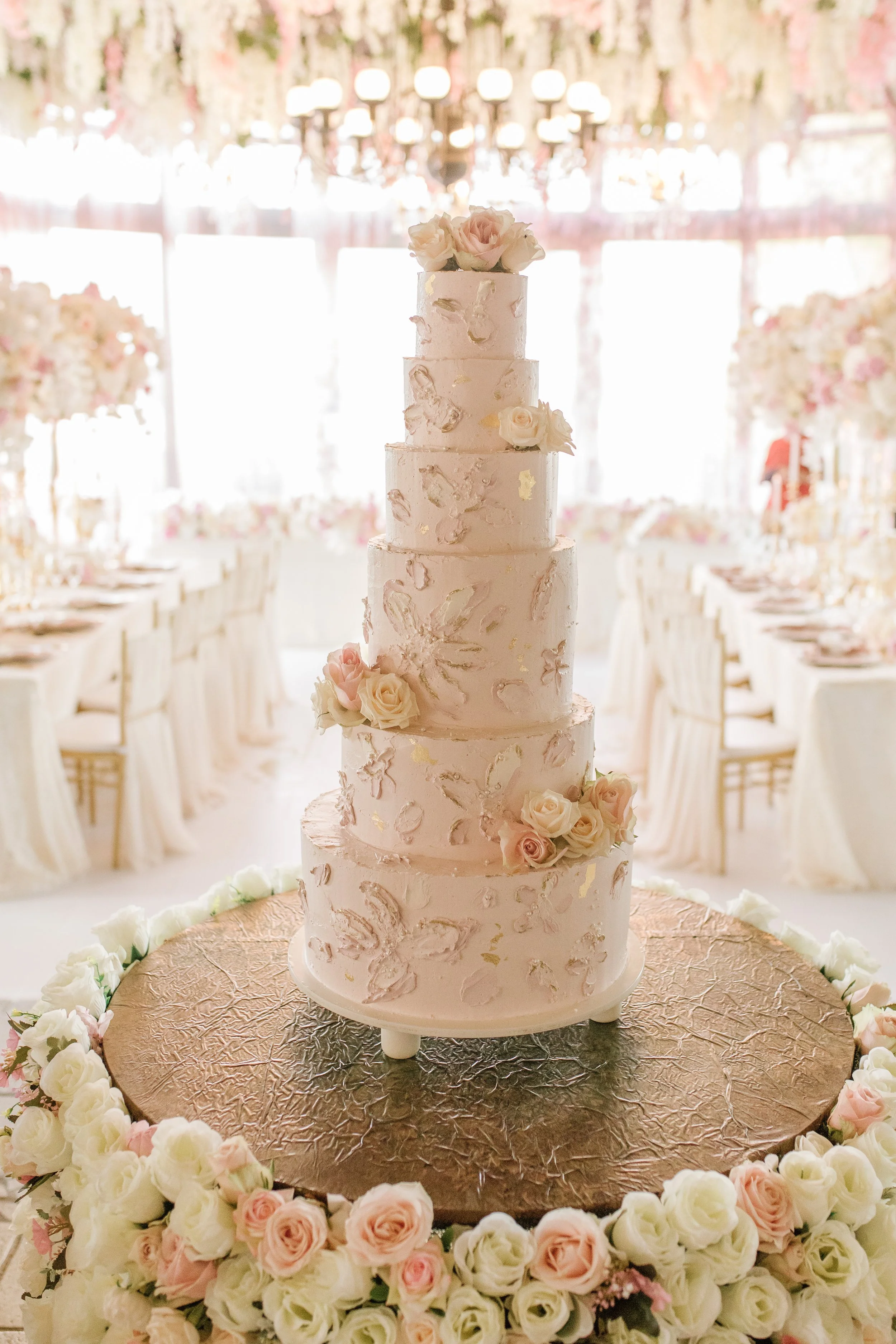 A 6-tier wedding cake styled on a large plinth with pink and white flowers