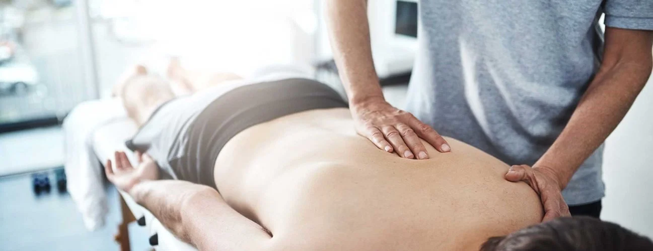 A man lying face down on a chiropractic table while a chiropractor adjusts his upper back