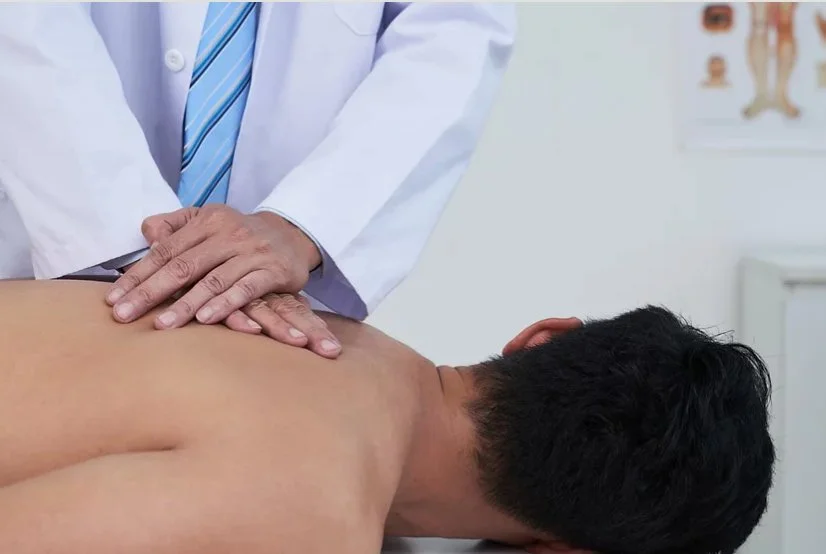 A man lying face down on a chiropractic table while a chiropractor adjusts his upper back