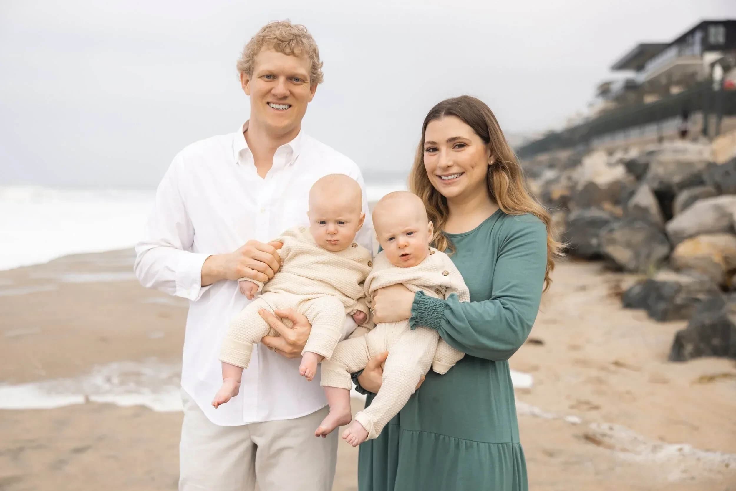 Dr. Derek and Dr. Caitlyn standing on a beach holding their twin sons