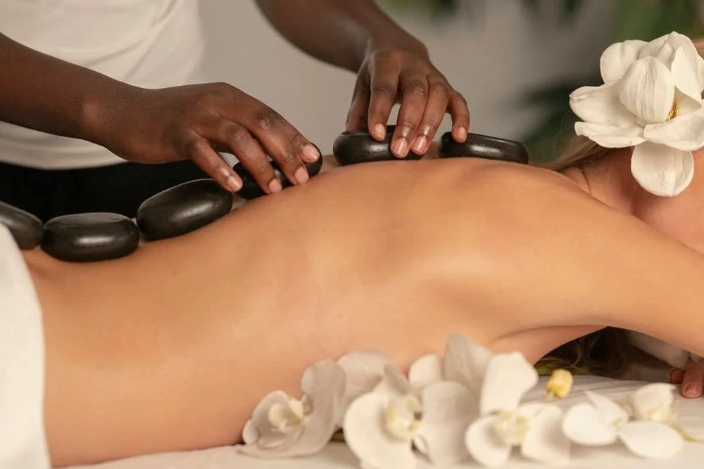 Person receiving a hot stone massage with white flowers nearby.