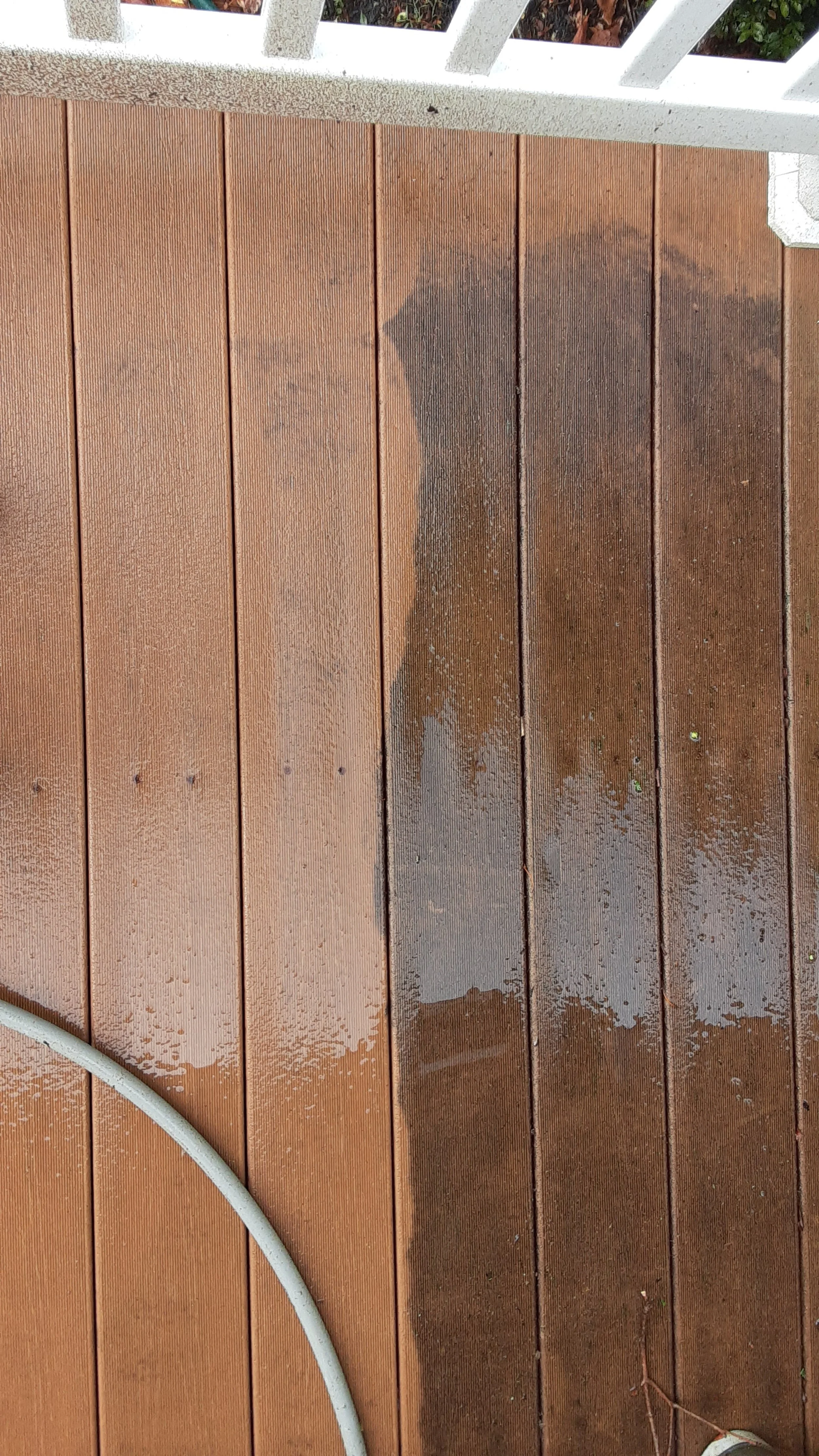 Wet wooden deck with a white railing at the top and a white garden hose in the bottom left corner.
