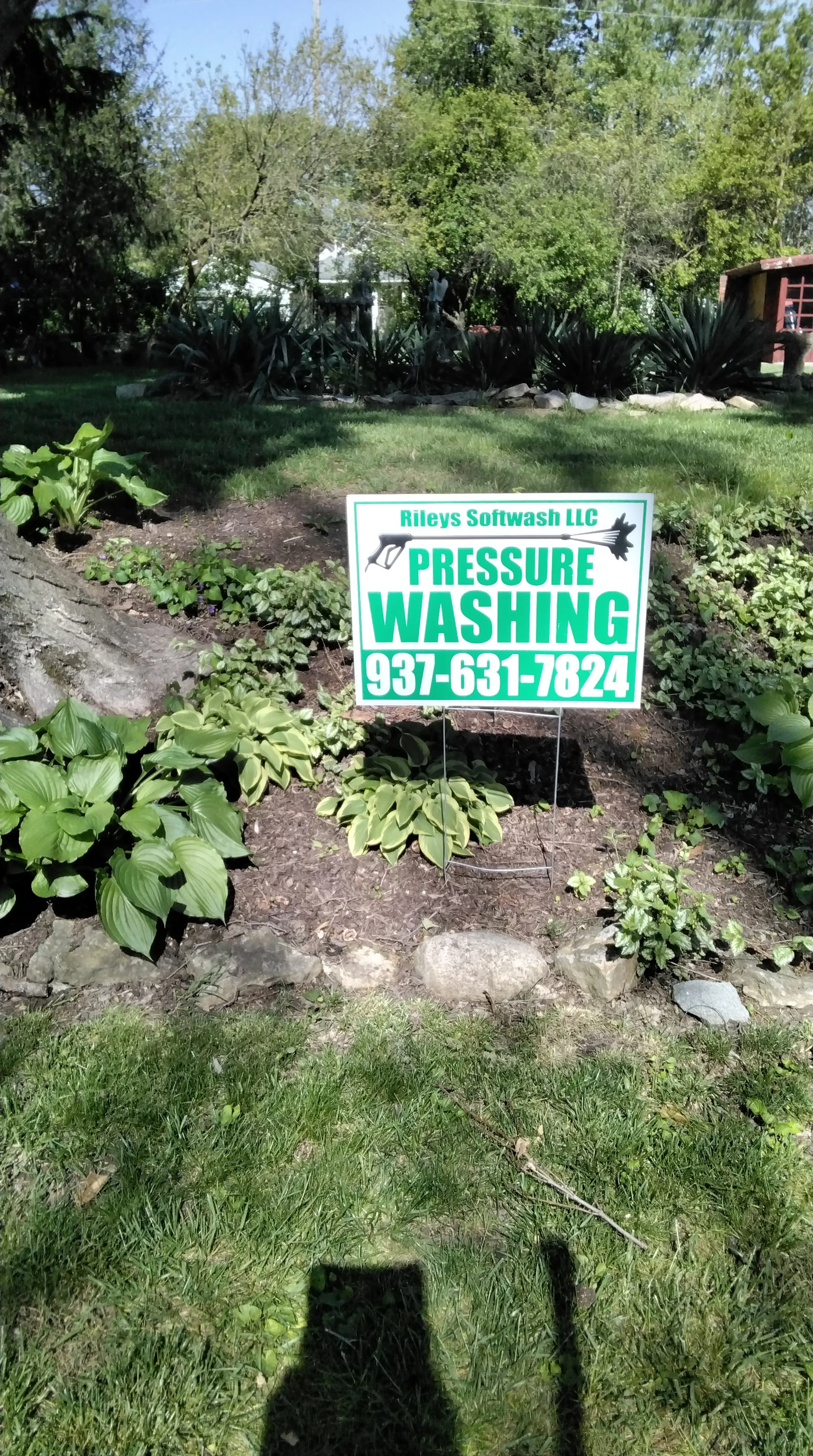 Sign advertising pressure washing services with a phone number in a garden with various plants and trees.