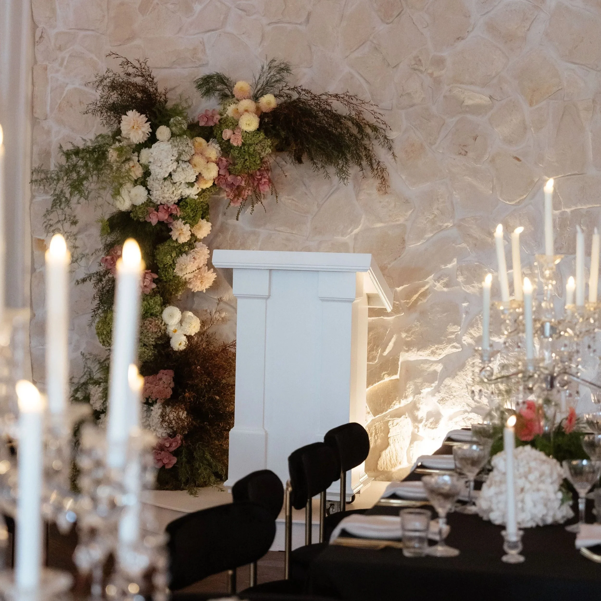 A floral arrangement with white, pink, and cream-colored flowers on a stone wall background, seen through a decorative white lattice