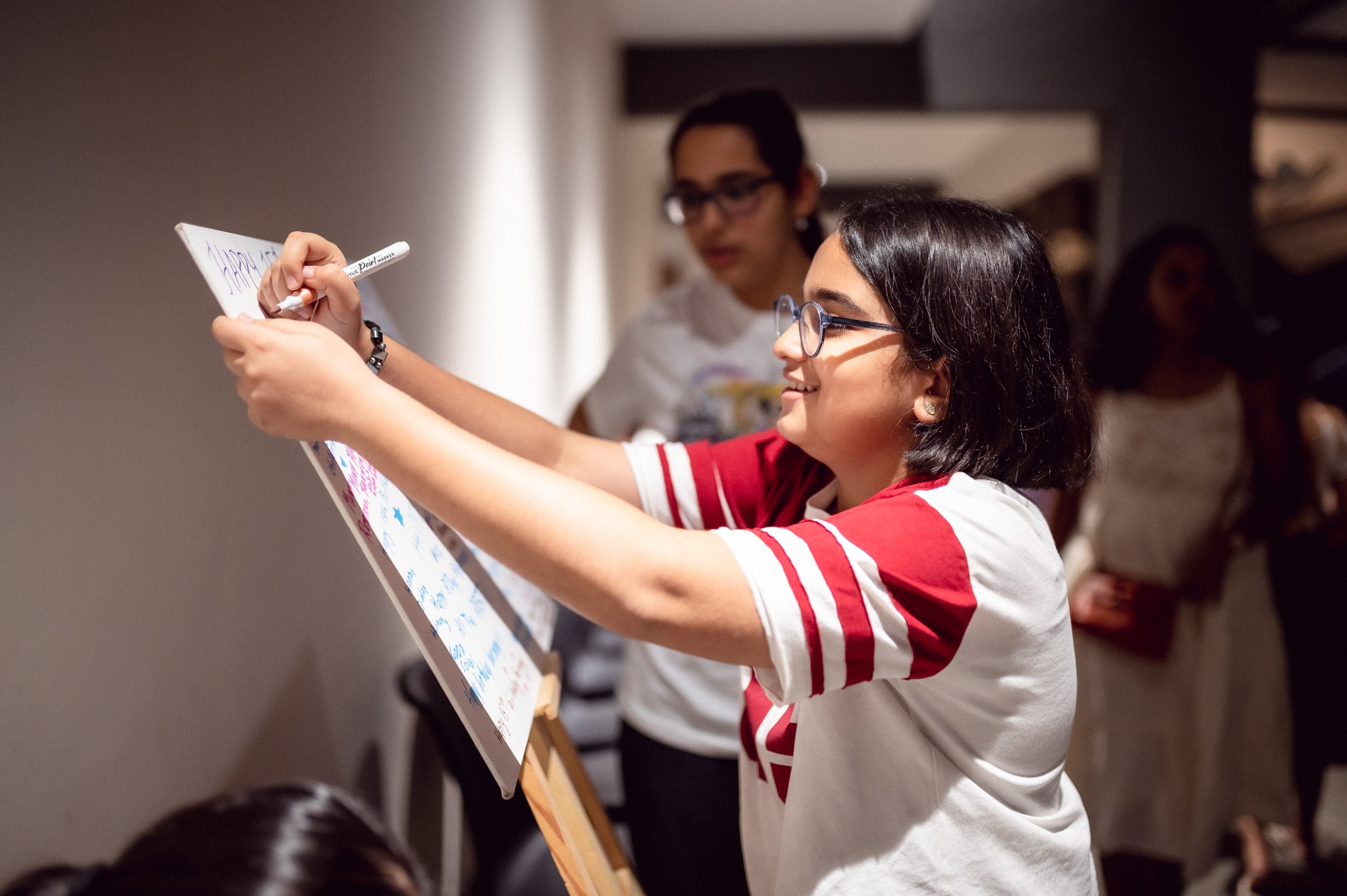 Smiling girl writes on a poster with a whiteboard marker.