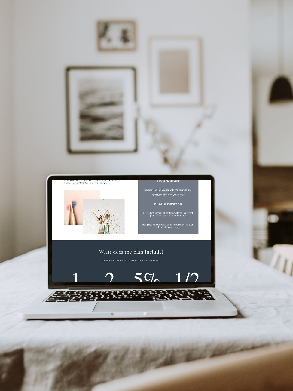 Laptop displaying a website about a dental plan on a white table in a bright room with framed pictures on the wall.