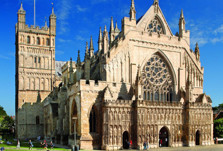Exterior view of a historic Gothic-style cathedral with ornate stonework, large stained glass windows, and a bell tower against a blue sky.