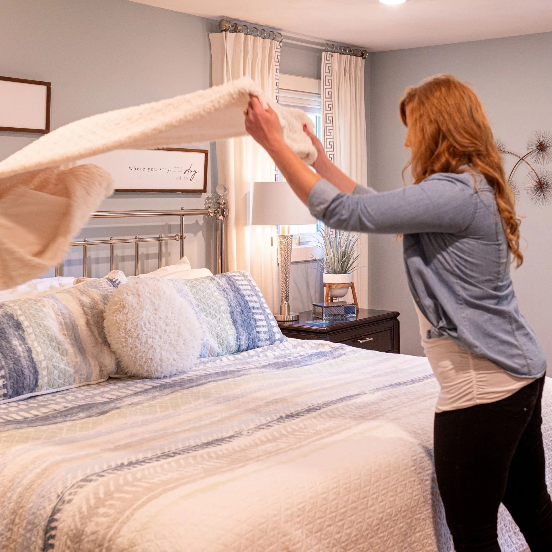 Home organizer smoothing out a clean comforter on a styled bed, demonstrating a peaceful and functional bedroom system reset.