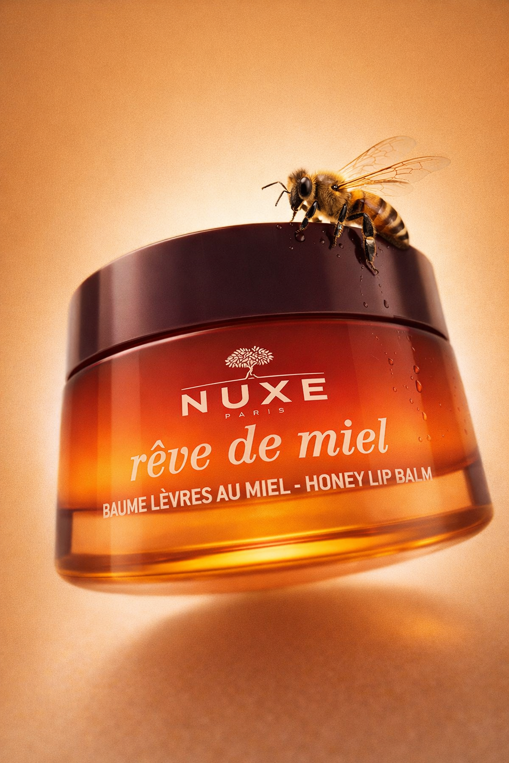 A honey bee sitting on top of a NUXE honey lip balm jar, with a warm, gradient background.