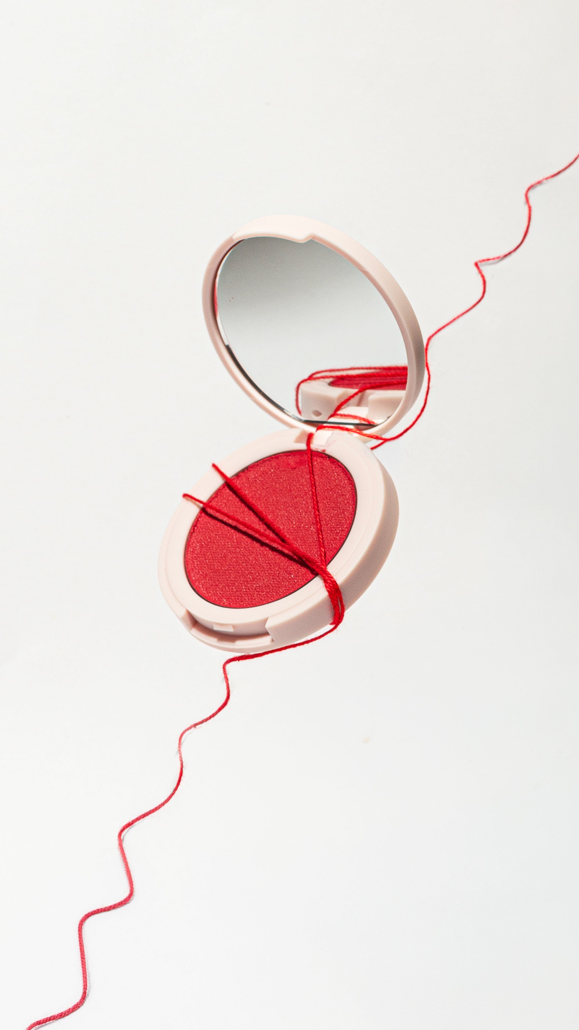 A Kylie Cosmetics blush with red thread in a minimalist setting.