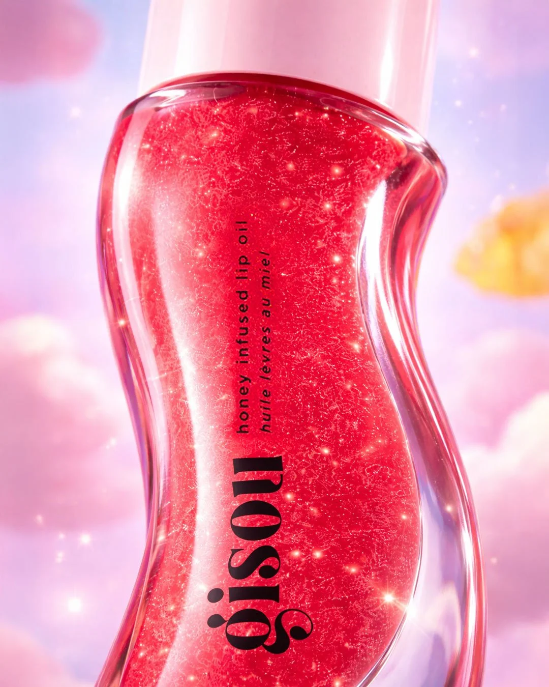 Close-up of a bottle of Gisou honey-infused lip oil with a pink cap, set against a pink and purple background with sparkles and blurred shapes.