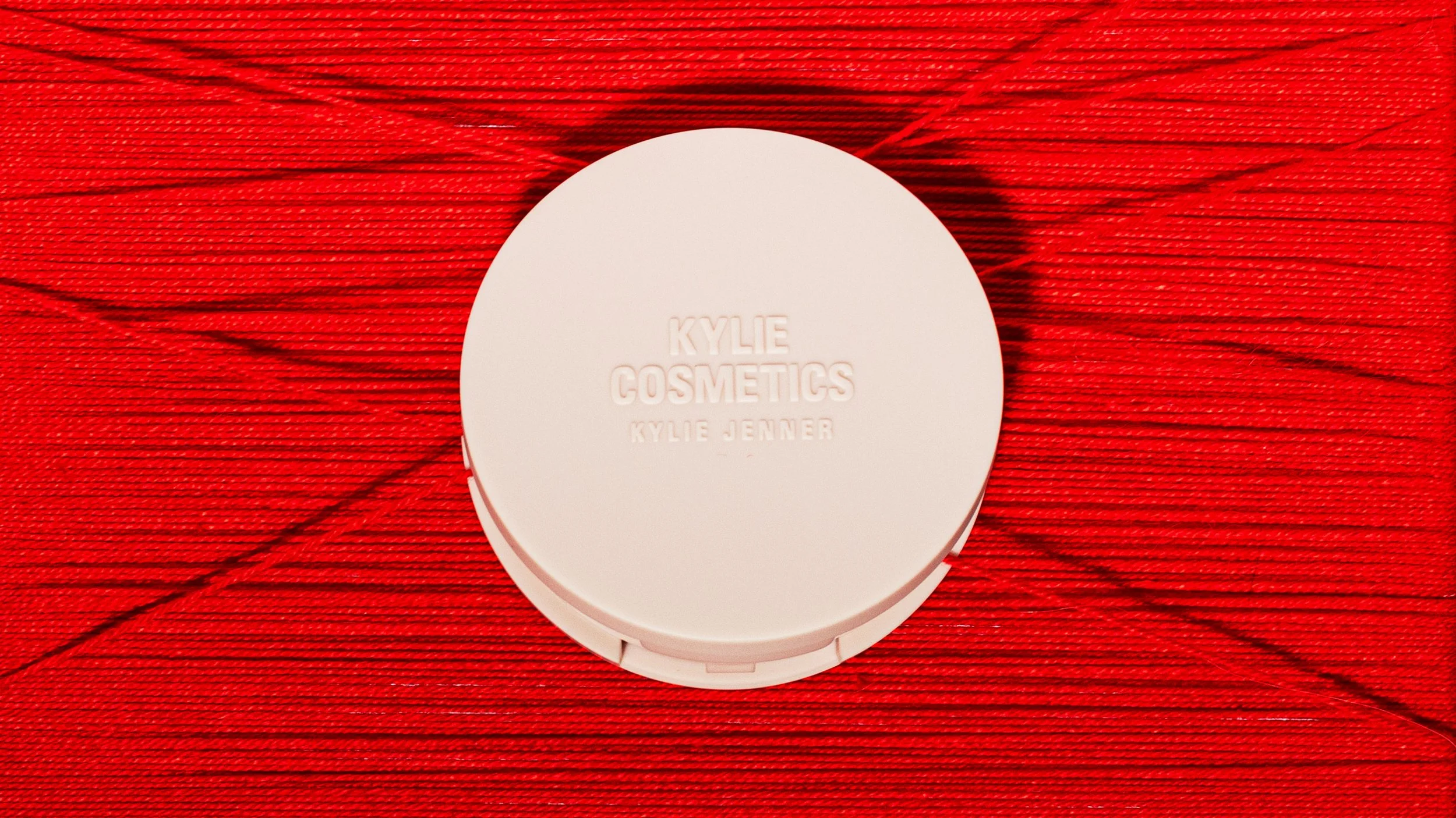 A blush embossed text that reads 'KYLIE COSMETICS KYLIE JENNER' sitting on a red textured surface.