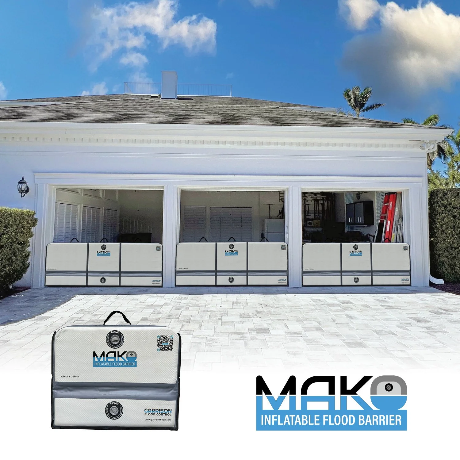 Inflatable flood barriers set up outside a house to prevent floodwater from entering. The barriers are white with blue and black branding, and are arranged along the house's open area, with a close-up of one barrier in front. The house has a white exterior and an open space revealing a living area and tools inside.