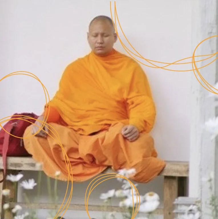 A Buddhist monk in orange robes sitting cross-legged on a wooden bench, eyes closed, in a peaceful meditation pose.