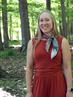 Photo of Teresa, our farm coordinator standing in a red dress in the forest