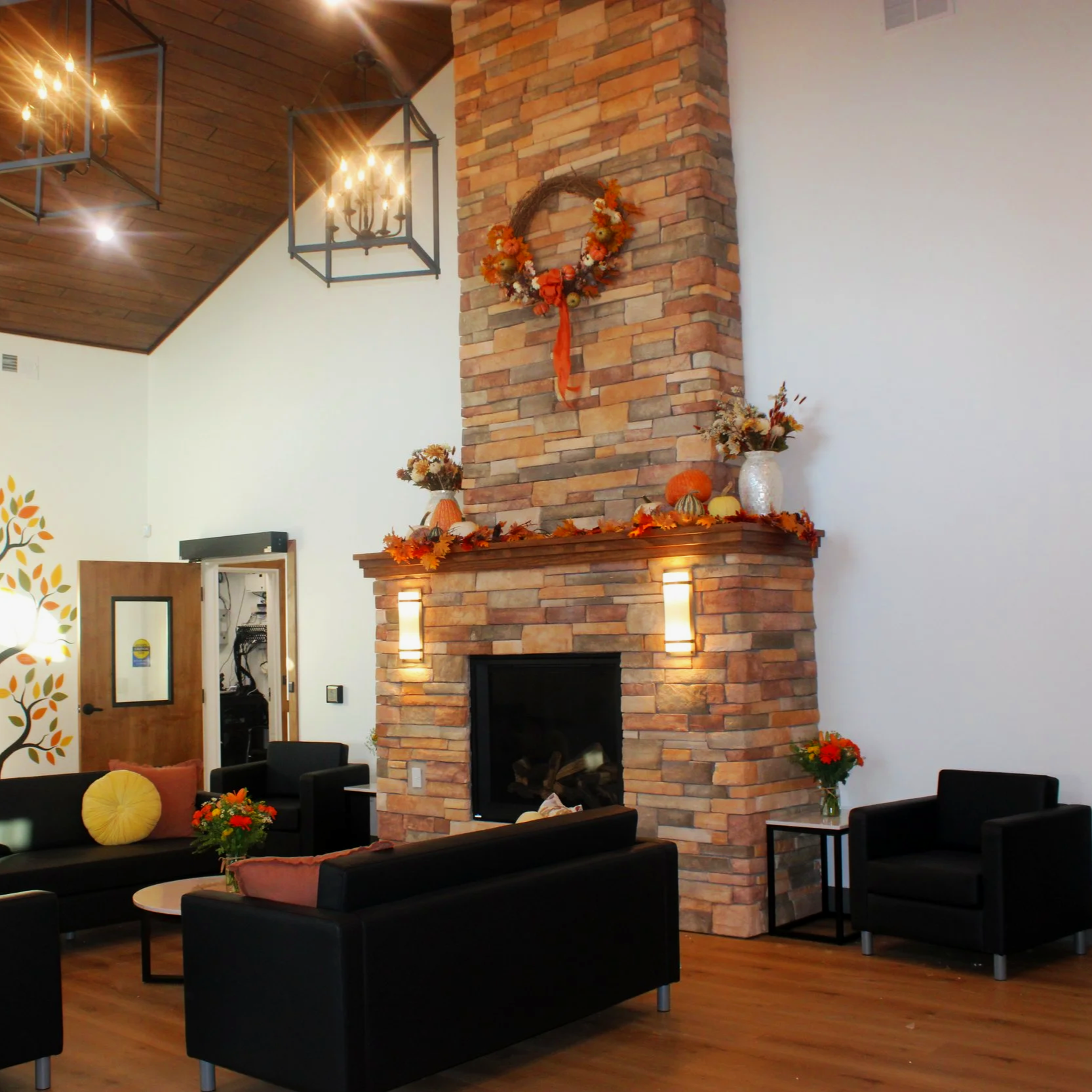 Photo of the main lobby, fireplace, seating, and chandeliers of the Black Water Acres building with fall decorations consisting of leaf garland, pumpkins and artistic gourds, and fresh floral arrangements.