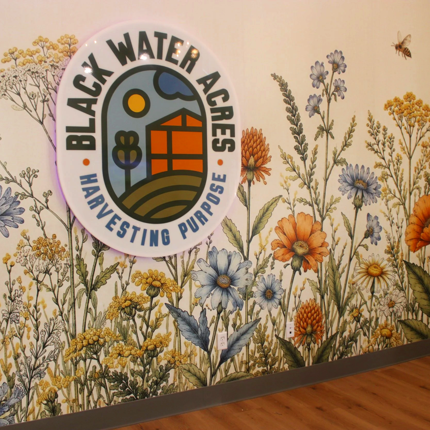 Black Water Acres logo with led backlighting on a large floral mural wall