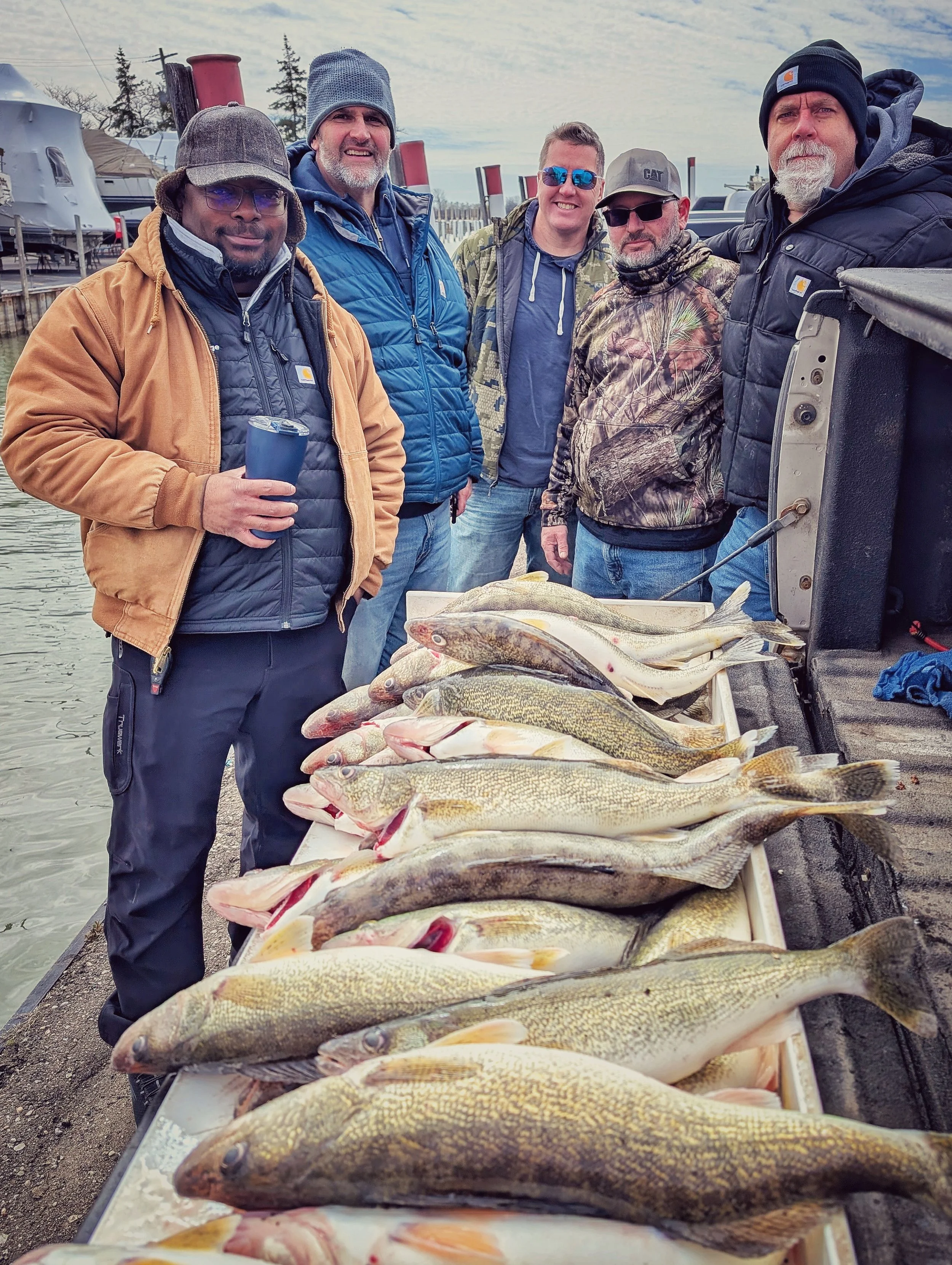  A group of five men standing behind a full limit of large walleye displayed on a tailgate after a successful spring fishing charter on the Detroit River with Reel Fish'n. 