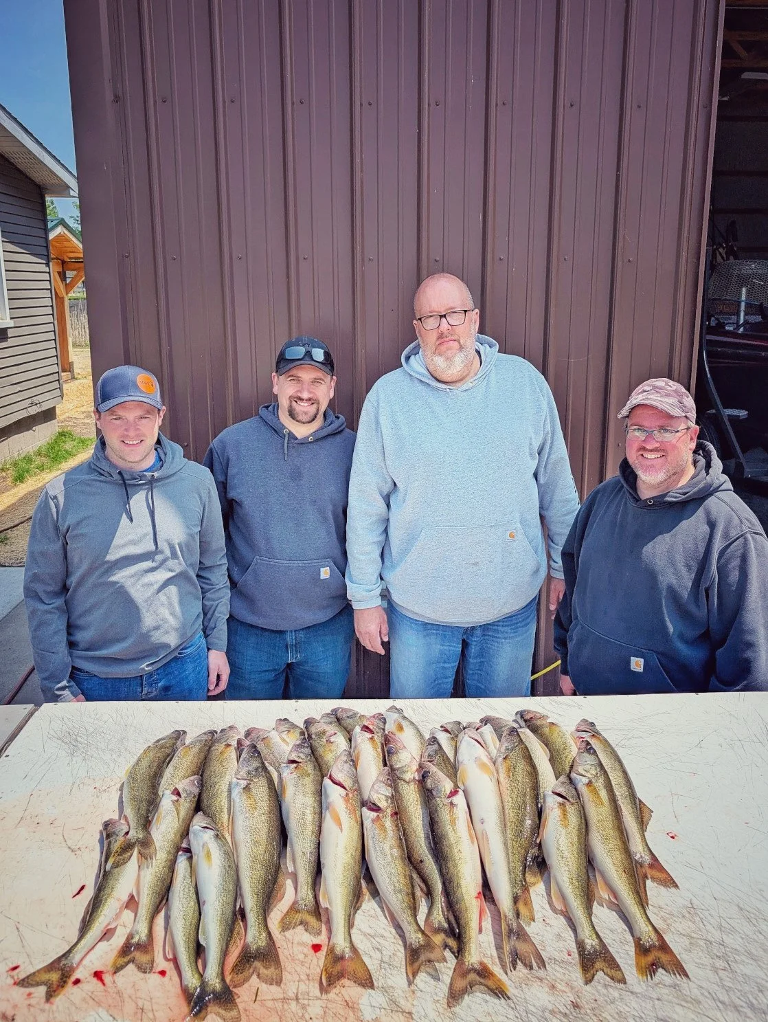  A group of four happy anglers standing behind a full limit of Saginaw Bay walleye laid out on a cleaning table after a successful Reel Fish'n charter out of Linwood, MI.   