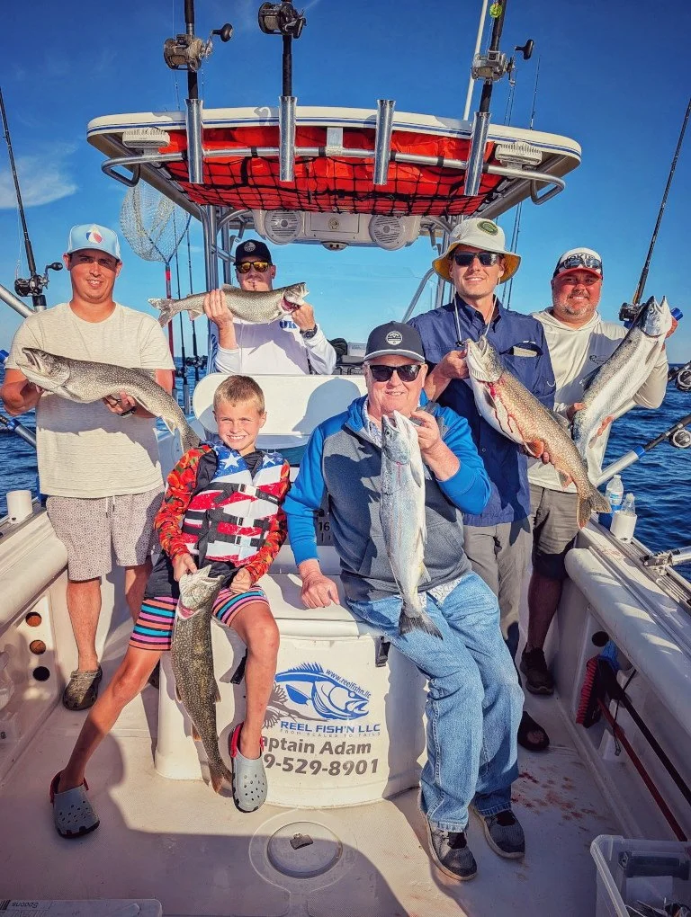  A group of anglers and kids displaying a mixed bag of Steelhead, Salmon, and Lake Trout on the deck of a Reel Fish'n charter boat in Oscoda. 