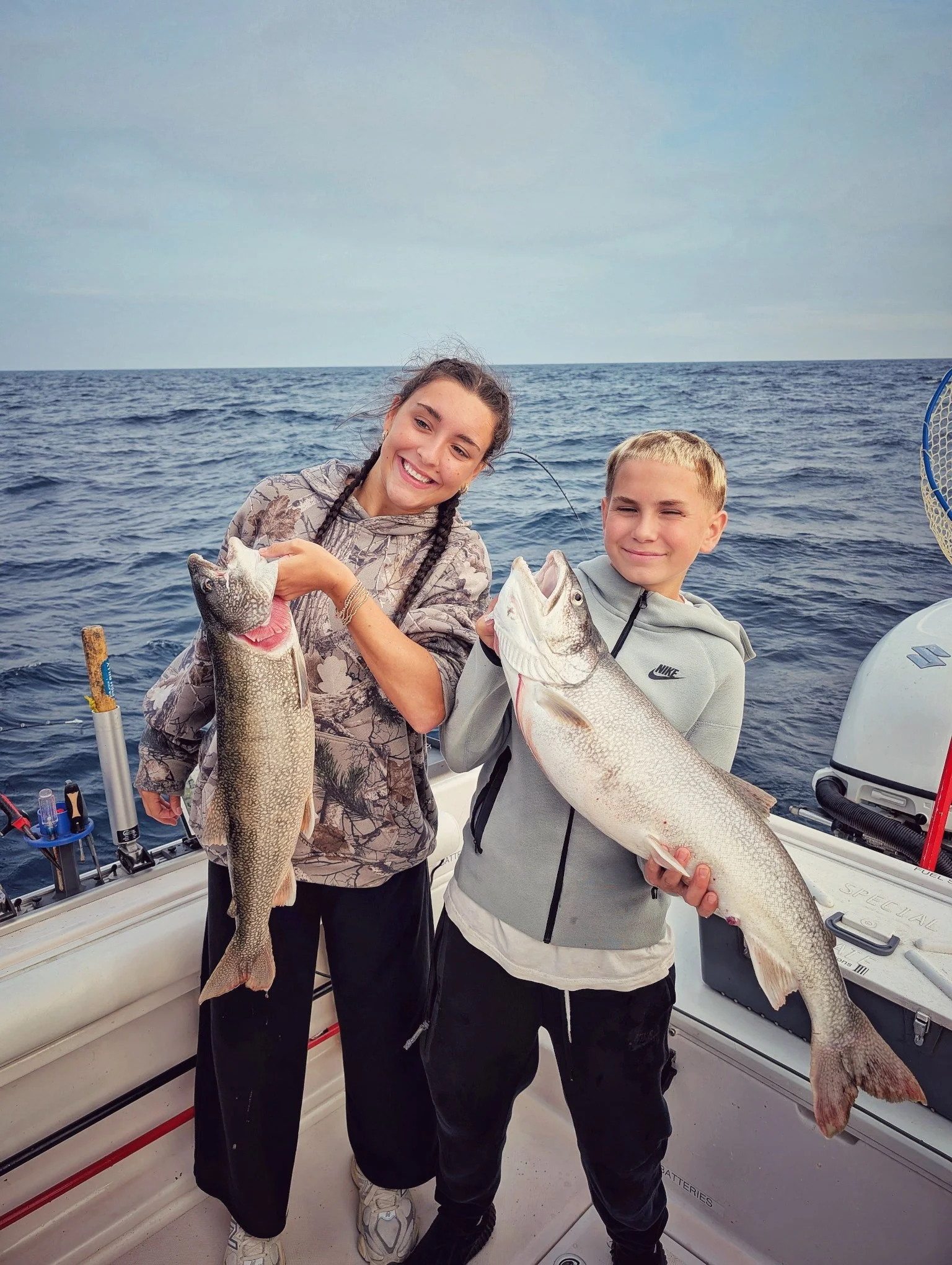  Two young anglers proudly holding up a pair of large Lake Trout caught on Lake Huron during a family-friendly fishing charter in Oscoda with Reel Fish'n. 